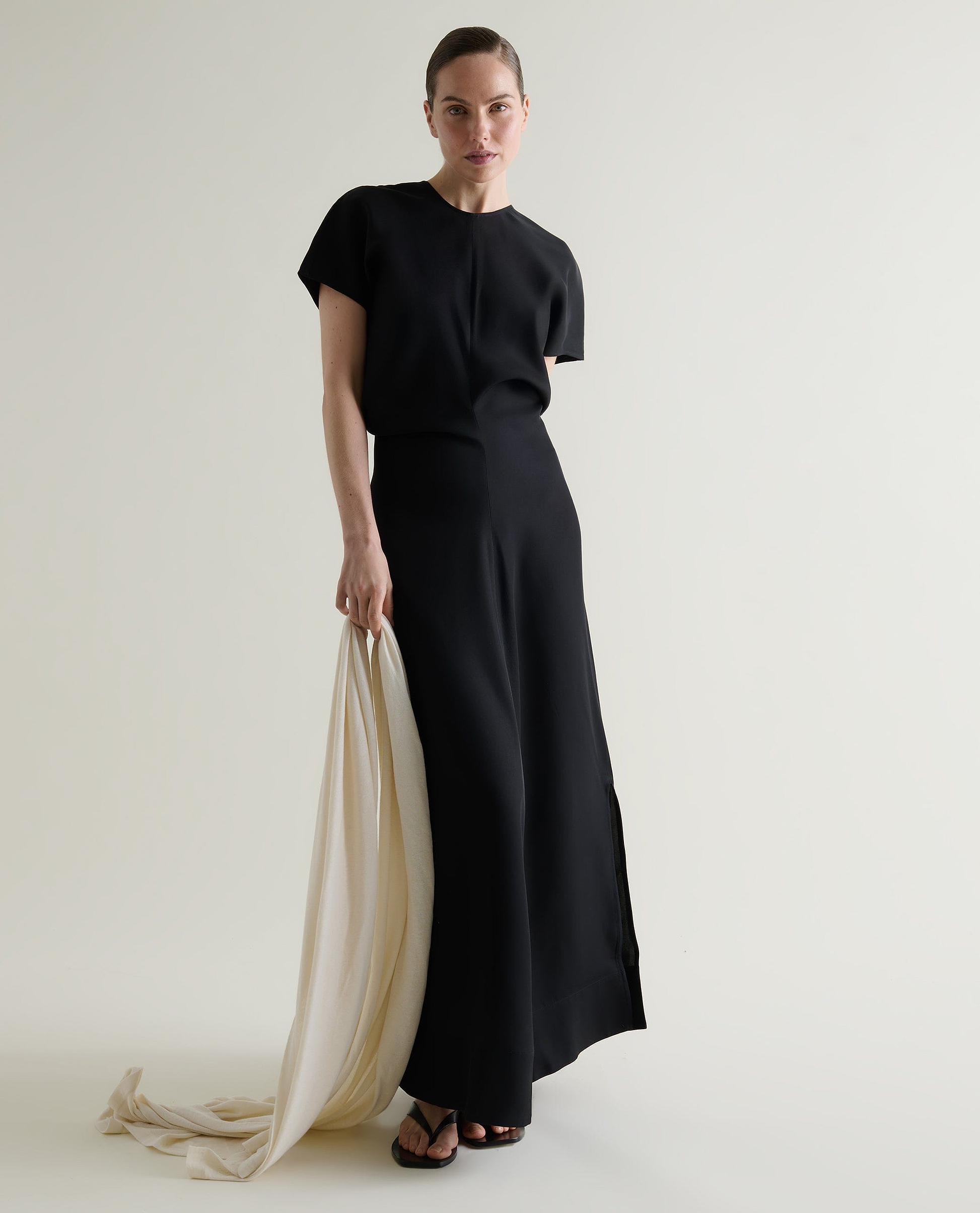 Woman wears black Naia maxi dress while holding a cream cashmere wrap.