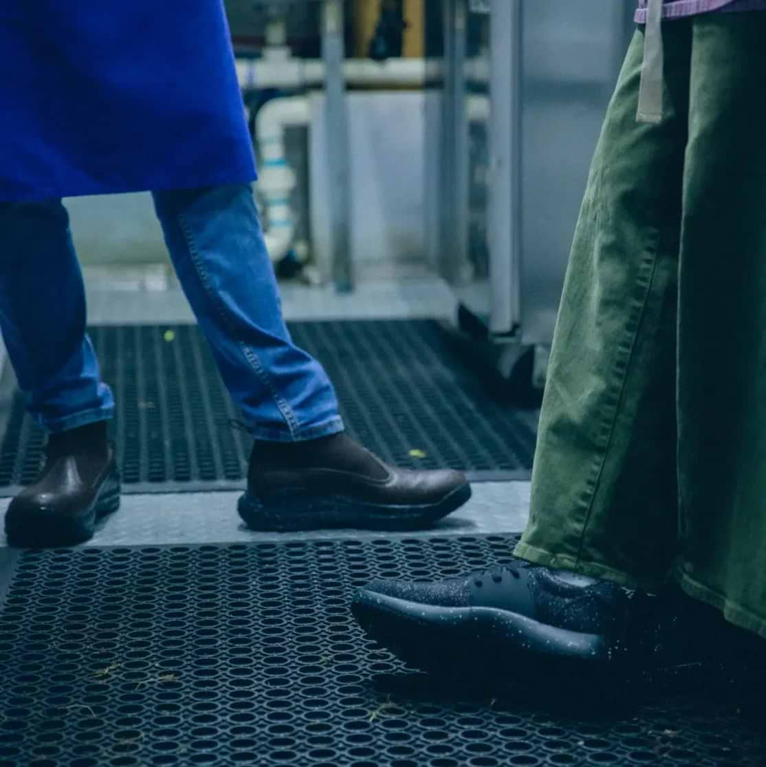 Person wearing black sneakers and gray pants standing on a floor with hair clippings.