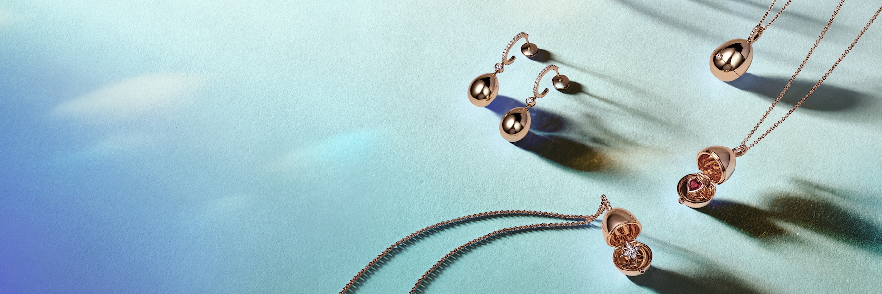 Fabergé Heritage surprise pendants and matching earrings in rose gold, featuring iconic egg-shaped designs with hidden gemstone surprises, displayed in an elegant luxury jewellery lay