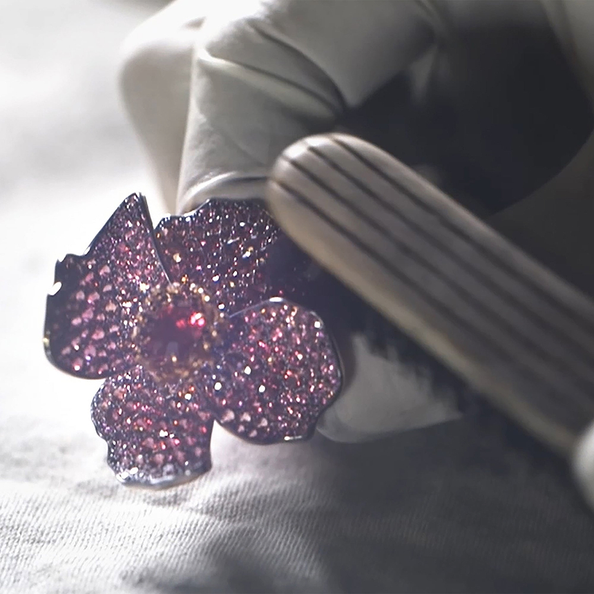 Close-up of Fabergé poppy brooch featuring pavé pink gemstones and a central red stone, held with jeweller’s tools during the craftsmanship process.