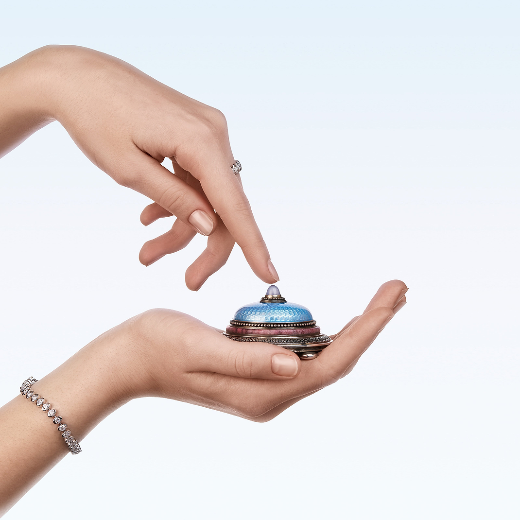 Hand holding a Fabergé enamel bell push object, styled with a Love by Fabergé diamond bracelet and diamond ring, showcasing exceptional craftsmanship and elegant jewellery design.