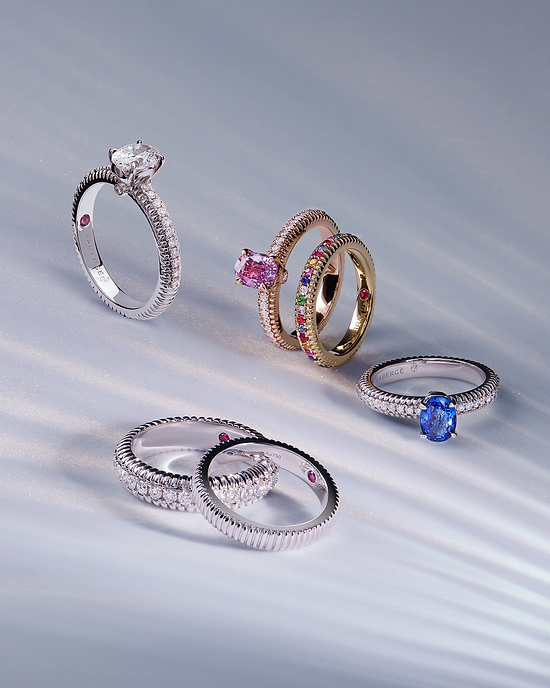 Flat lay of Fabergé Love Collection diamond and gemstone rings featuring sapphire, pink gemstone, and rainbow pavé designs on a soft light background.
