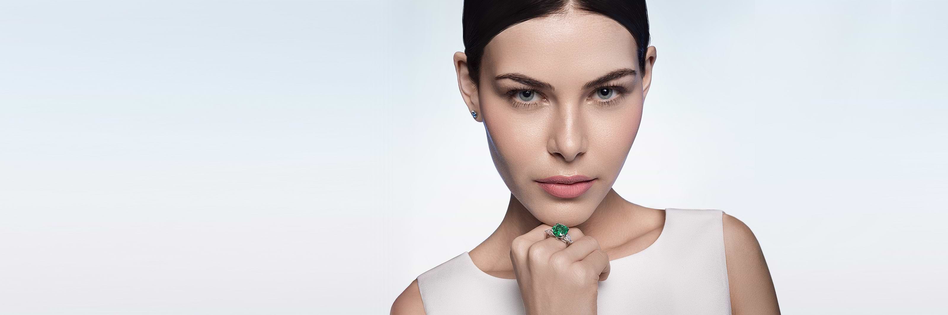 Woman wearing a Fabergé emerald ring on a light gray background