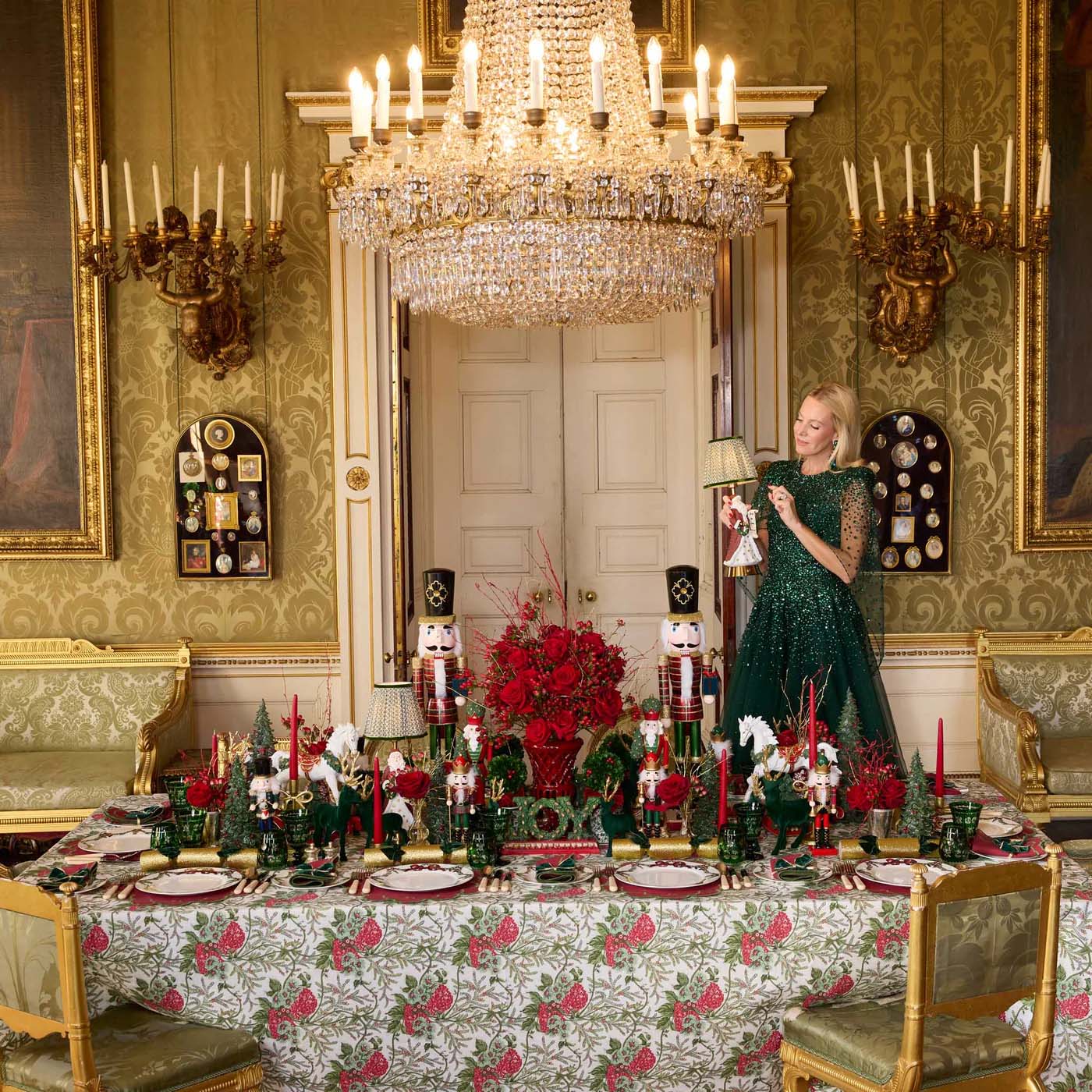 Decorative dining room with a woman in a green dress, ornate chandelier, and festive table setting.