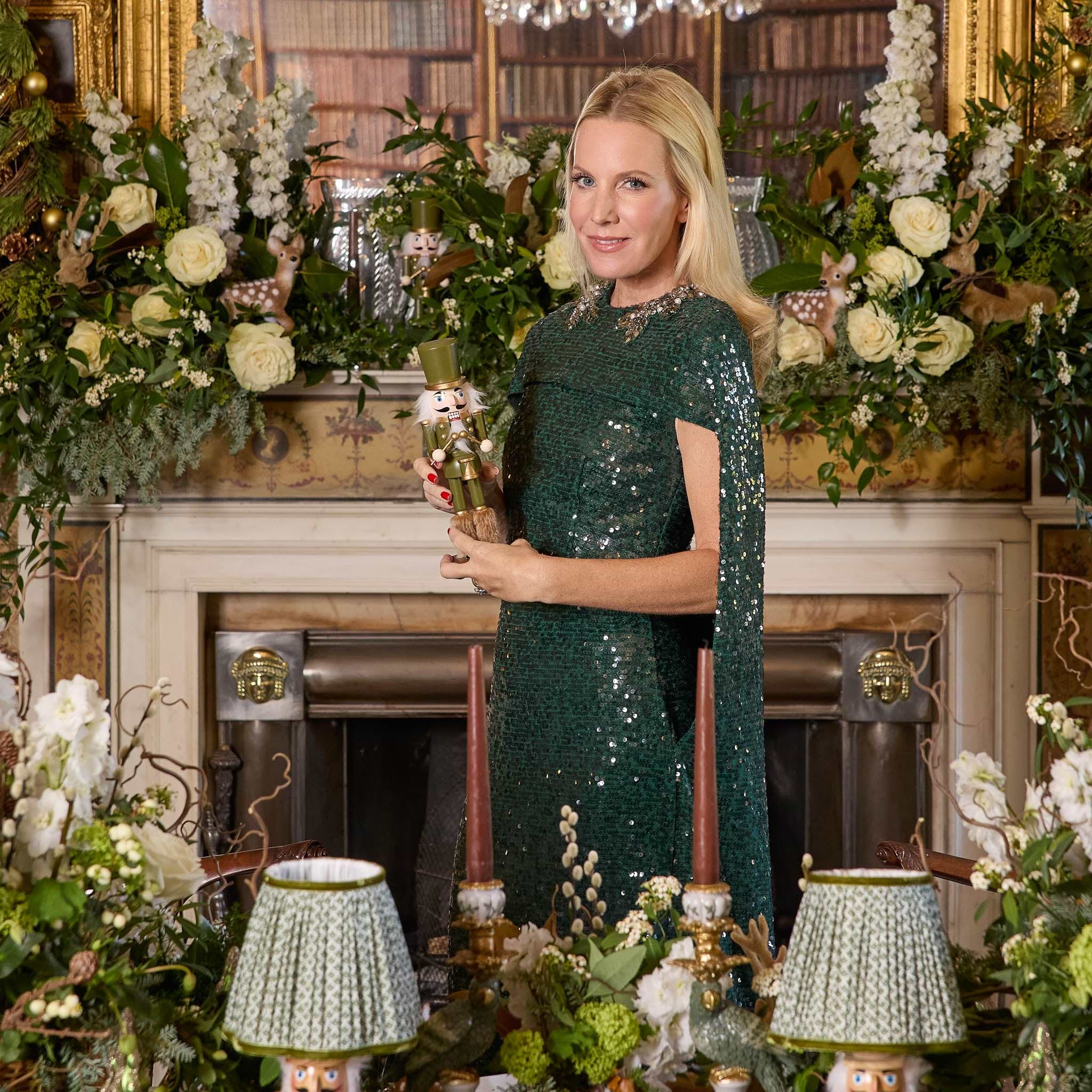 Mrs Alice in a green sequined dress holding a nutcracker, surrounded by floral decorations and lamps.