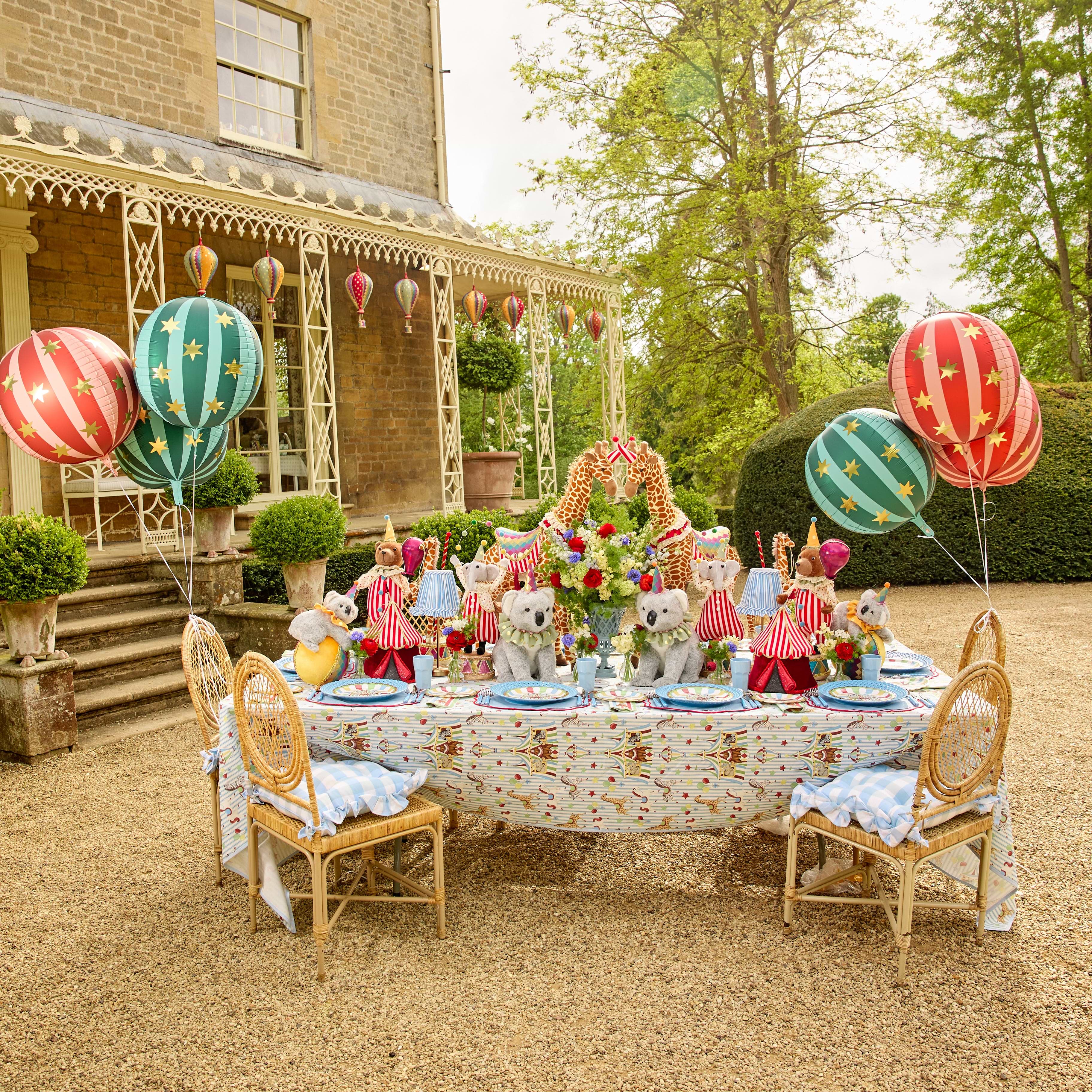 Decorated outdoor table with balloons and children's toys in a garden setting.