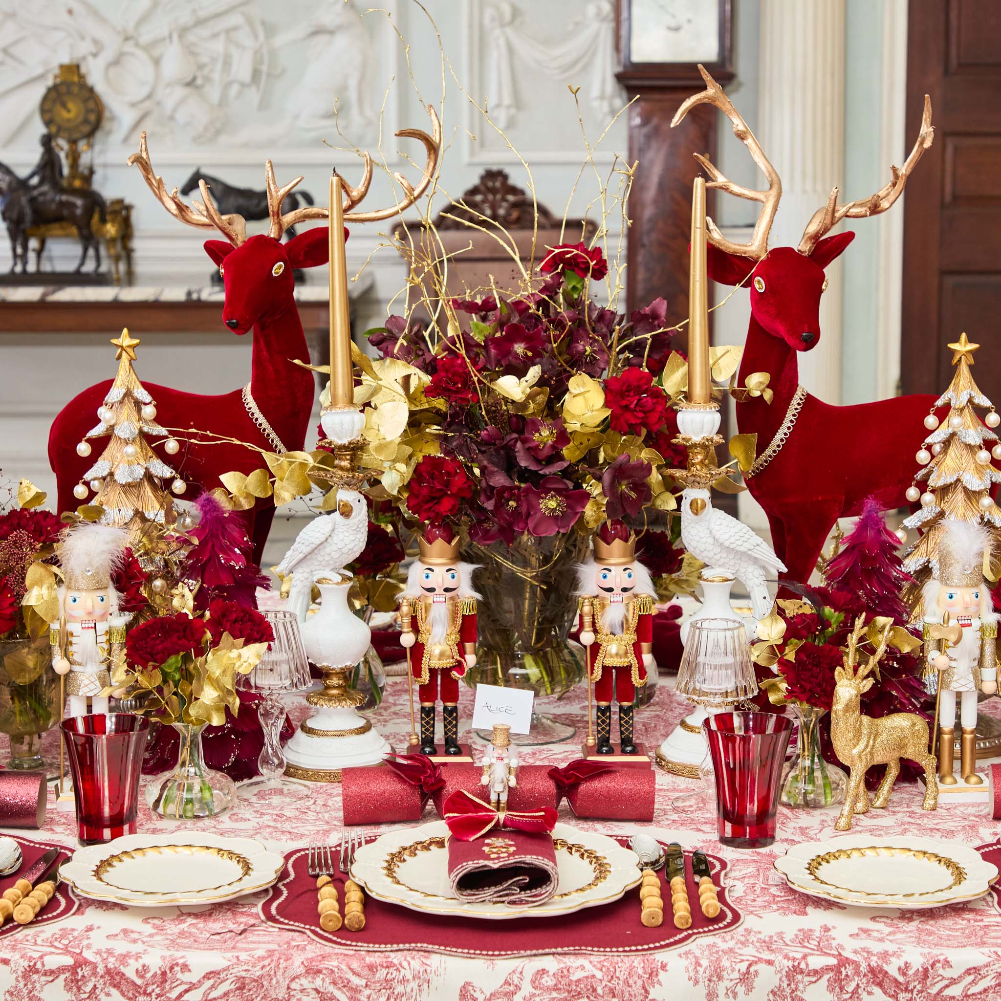 Decorative Christmas table setting with red and gold elements, including reindeer, nutcrackers, and floral arrangements.