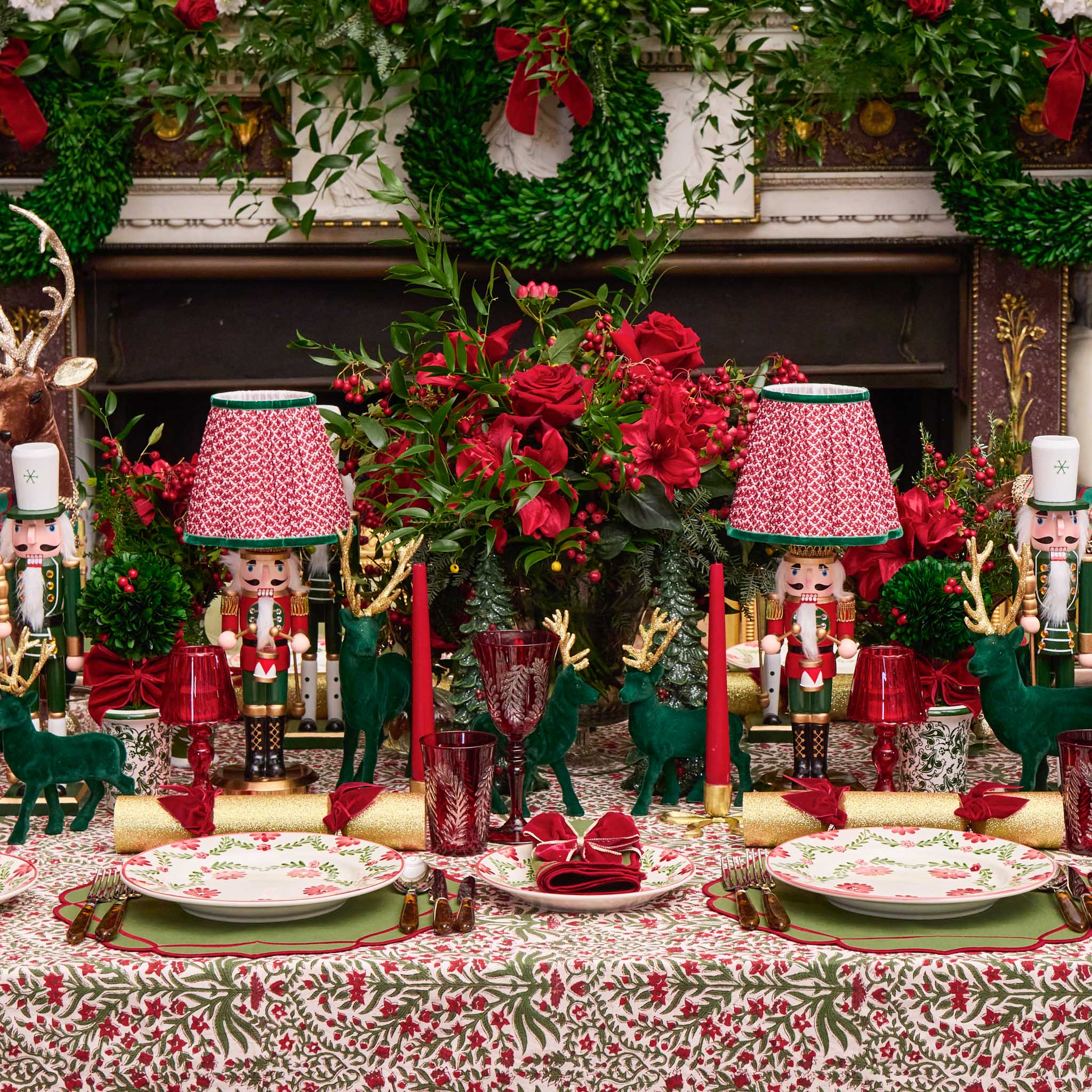 Decorative Christmas table setting with red and green theme, including flowers, nutcrackers, and tableware.