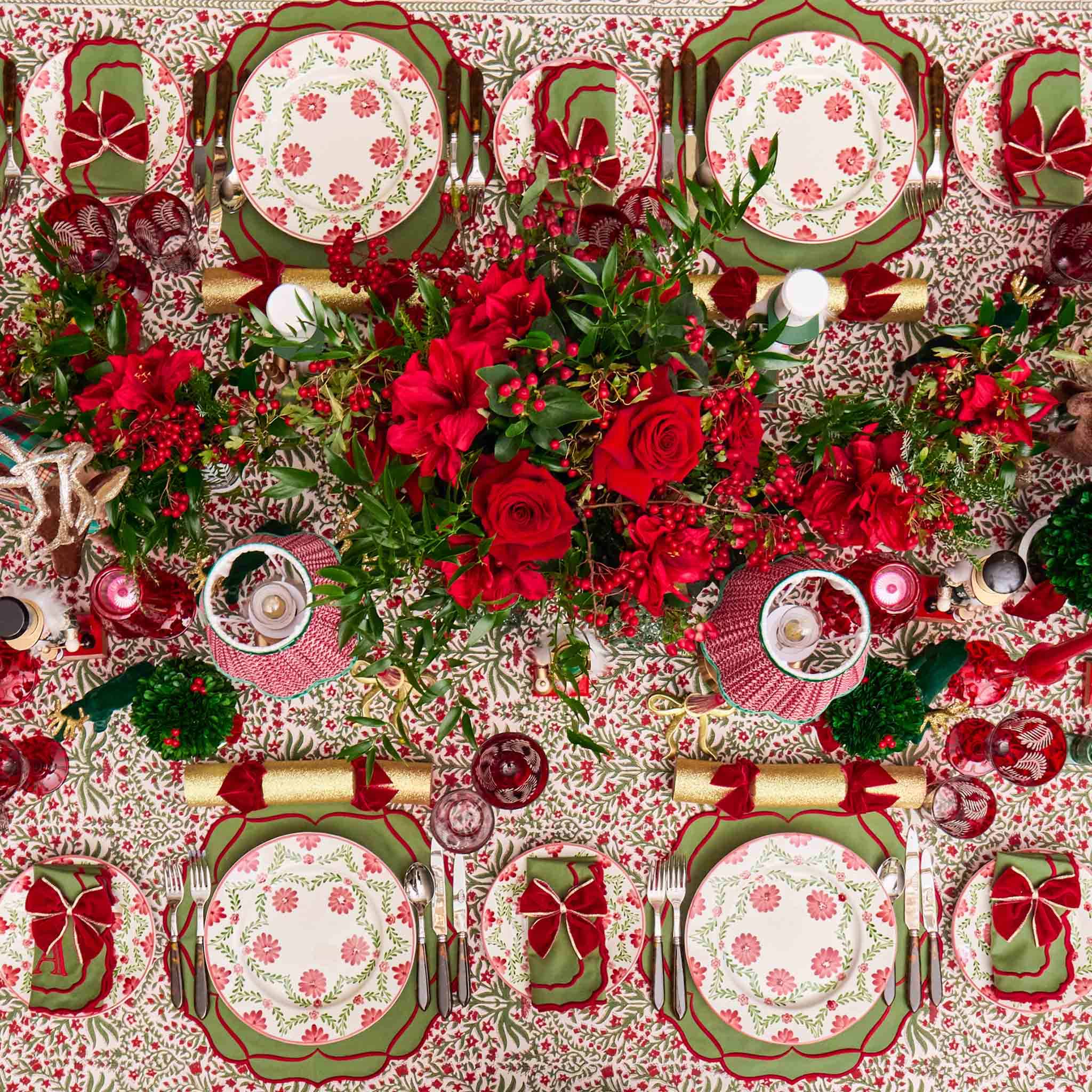 Decorative Christmas table setting with red and green floral patterns on plates and tablecloth.