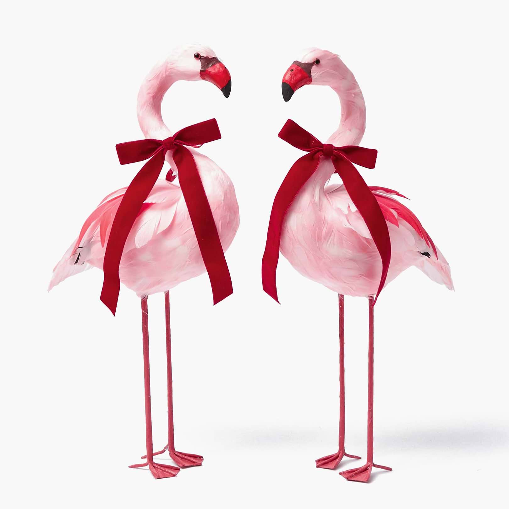 A pair of pink flamingo figurines with red velvet bows around their necks.