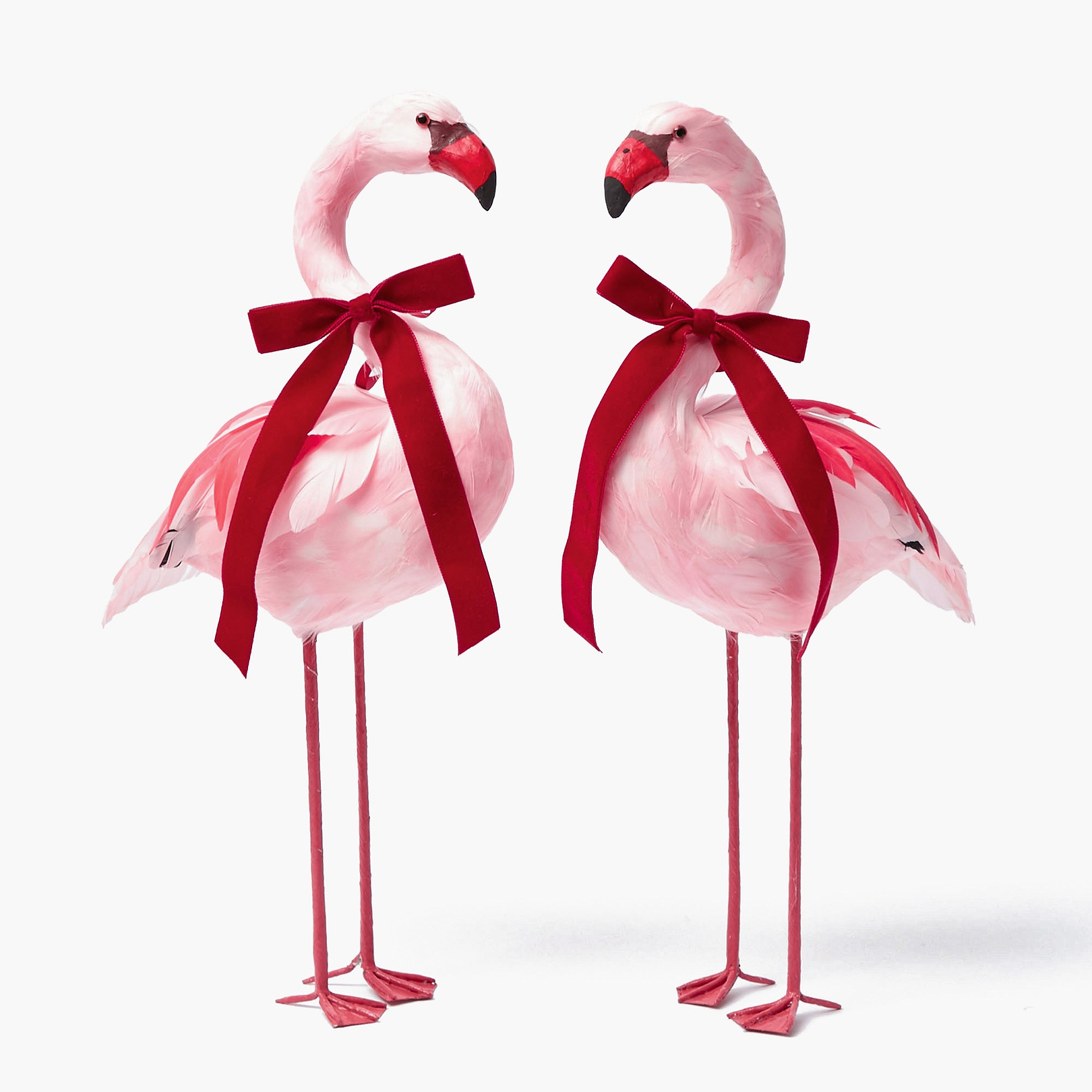 A pair of pink flamingo figurines with red velvet bows around their necks.