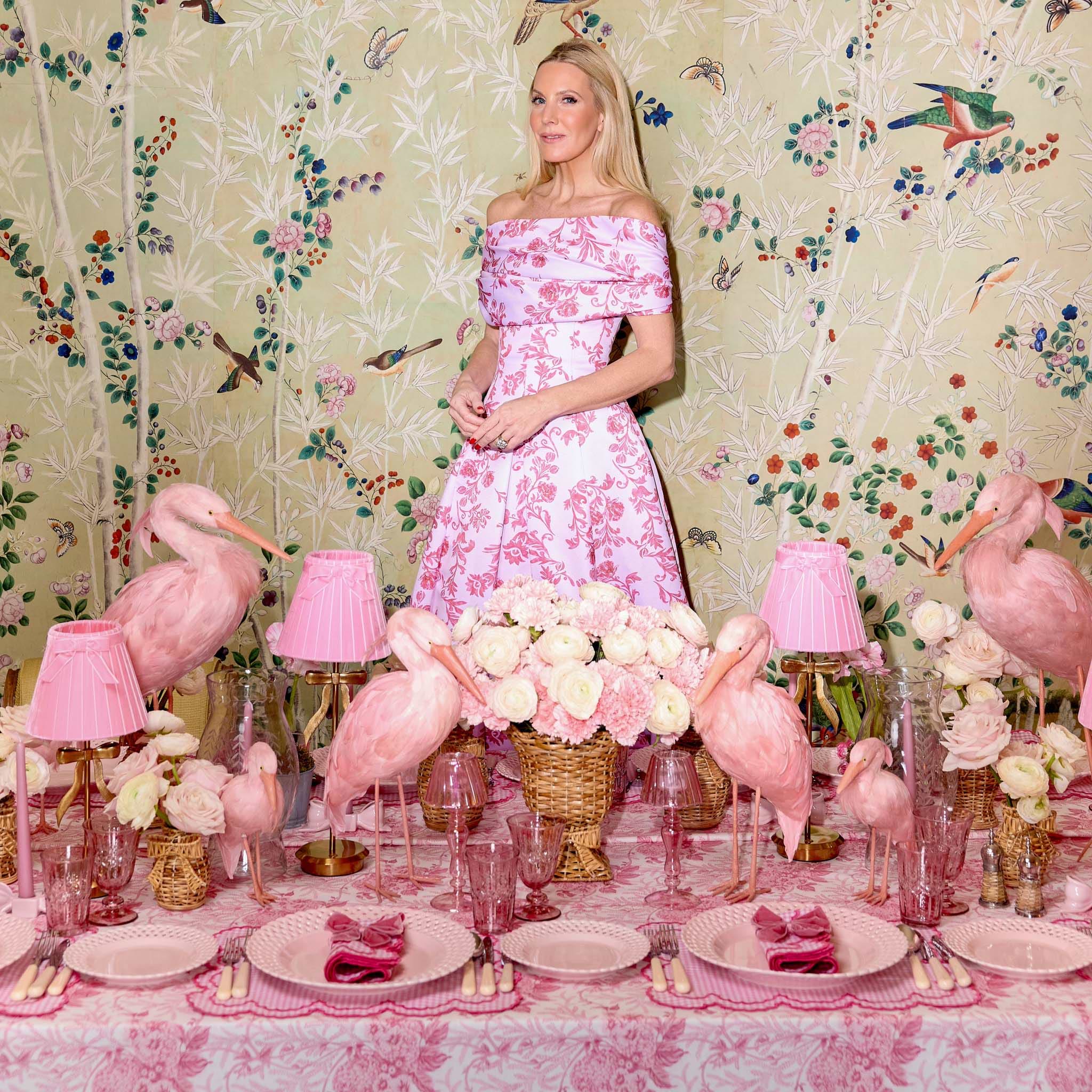 Woman in a floral dress standing behind a table with pink flamingo decorations and floral arrangements.