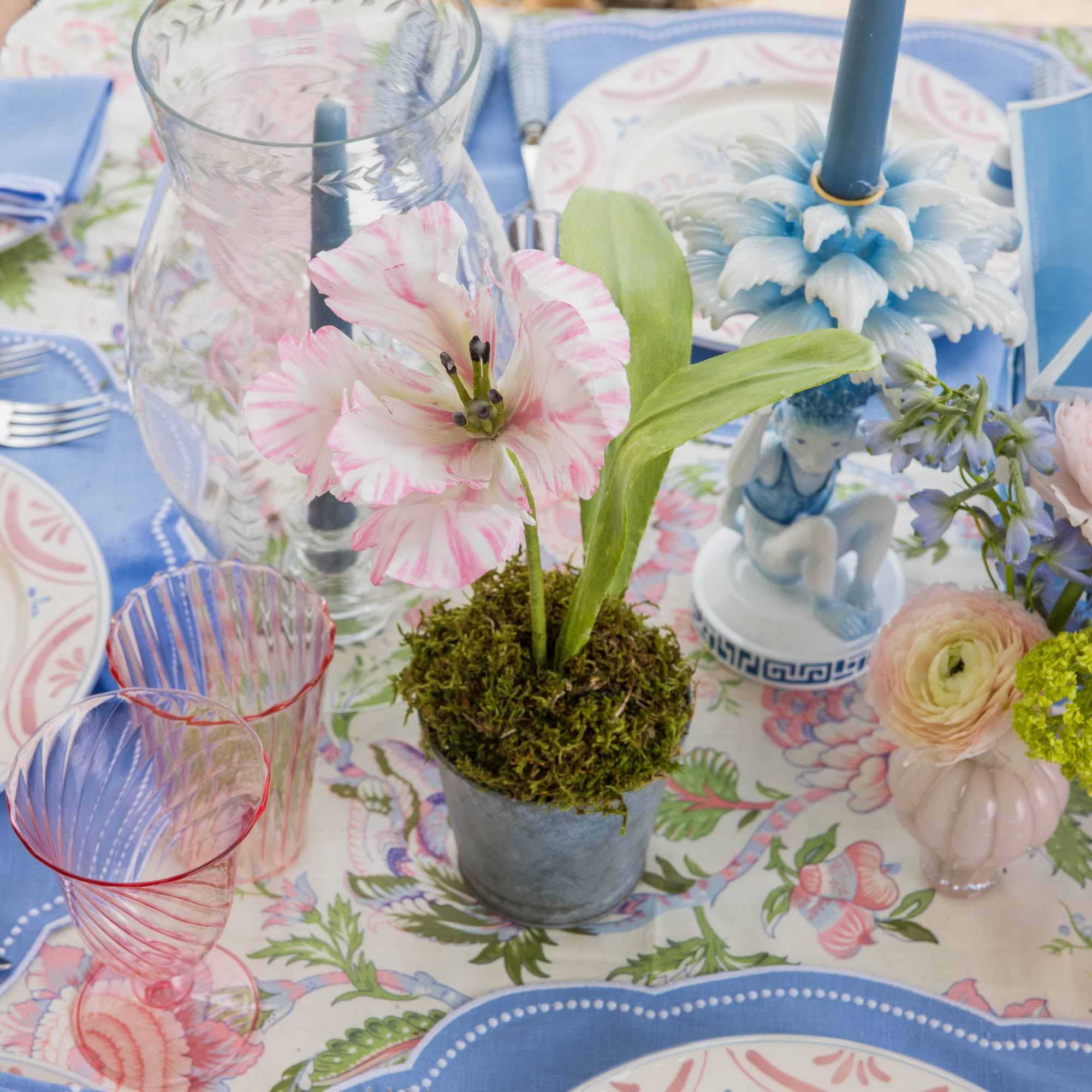 Decorative table setting with flowers, glasses, and a cake on a floral tablecloth.