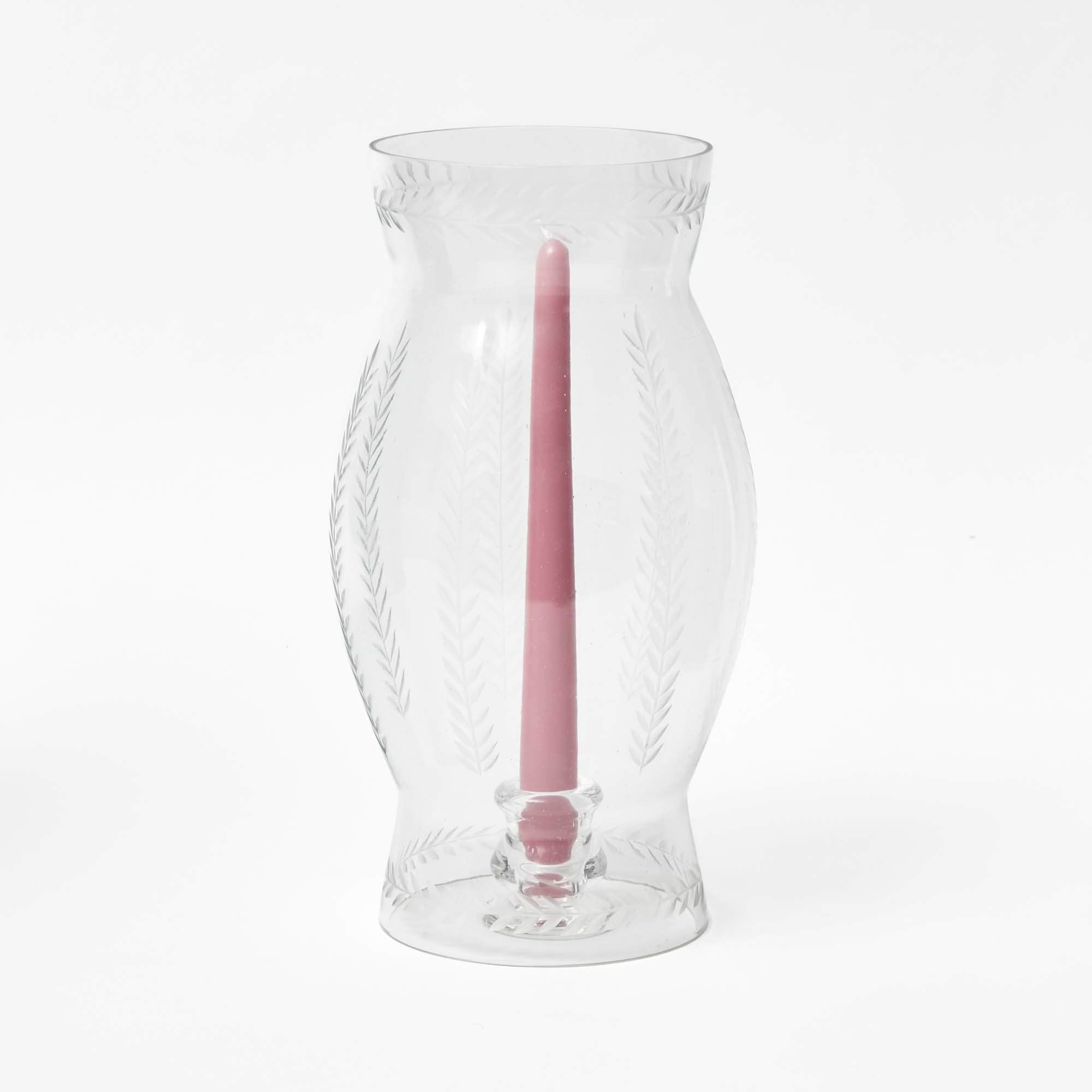 A clear glass lantern with engraved laurel leaf details, containing a pink candle.