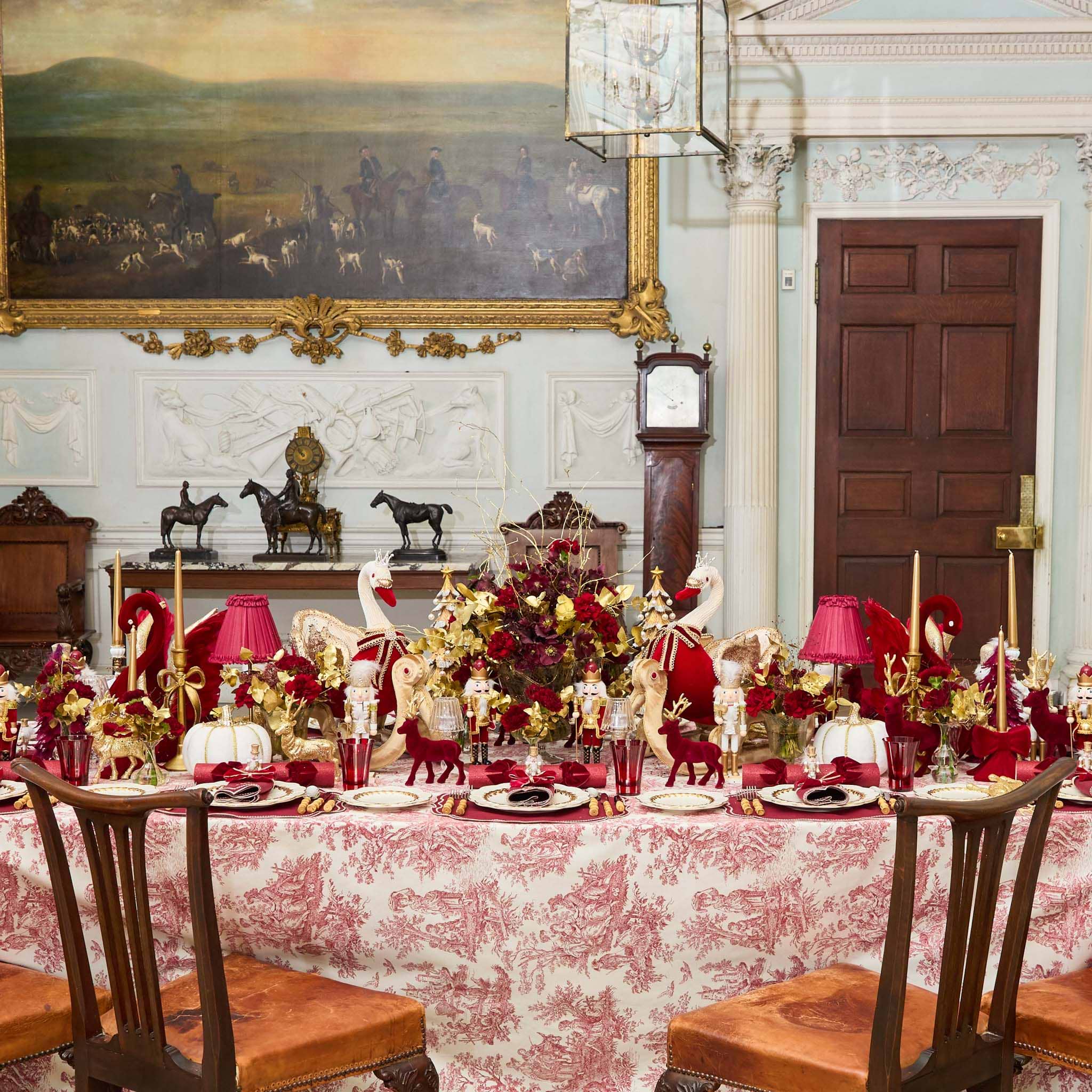 Decorative dining table set with red and gold tableware in a stately room.