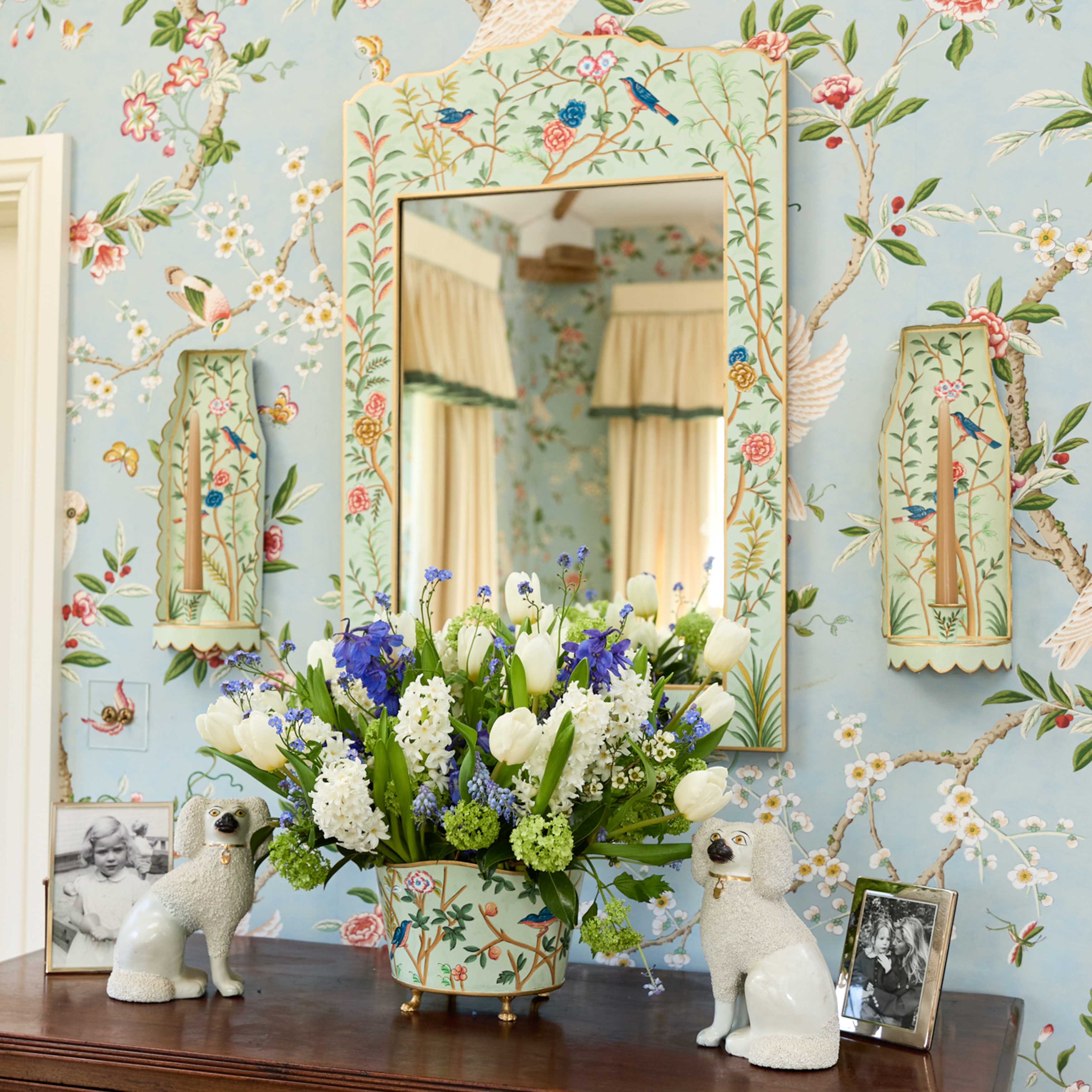 Decorative room with floral wallpaper, mirror, and floral arrangement on a table.
