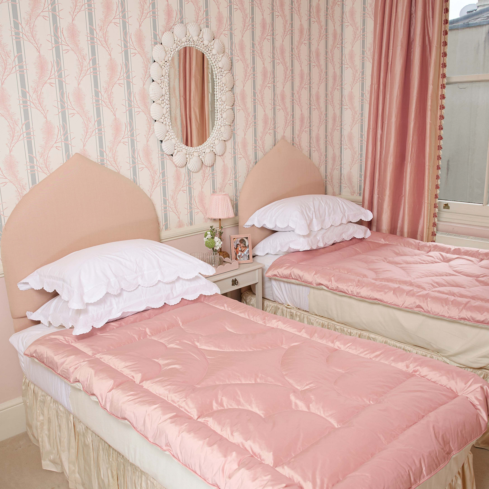 Two twin beds with pink bedding in a room with striped wallpaper and a mirror.