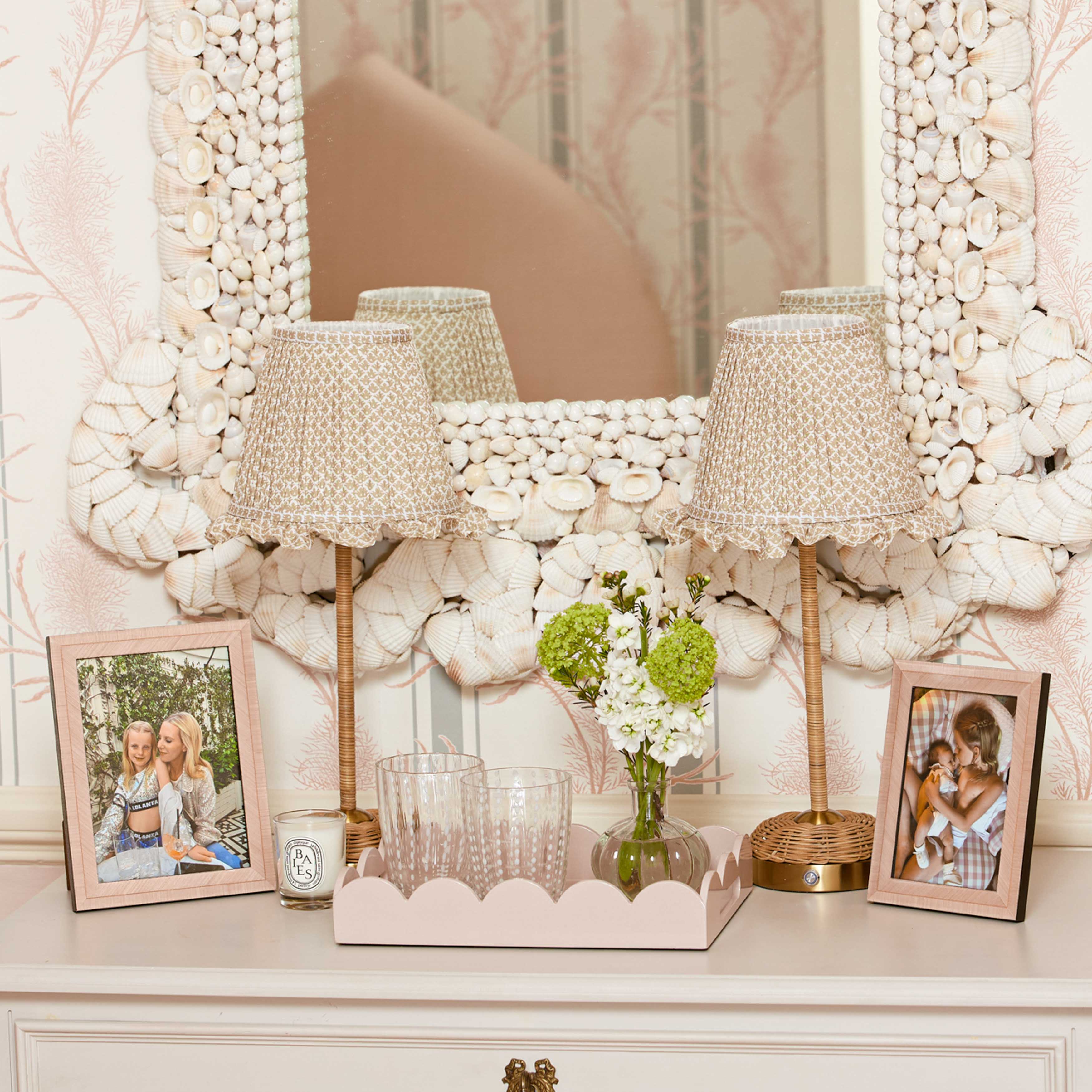 Decorative table setting with lamps, photos, and a vase in front of a decorative mirror.