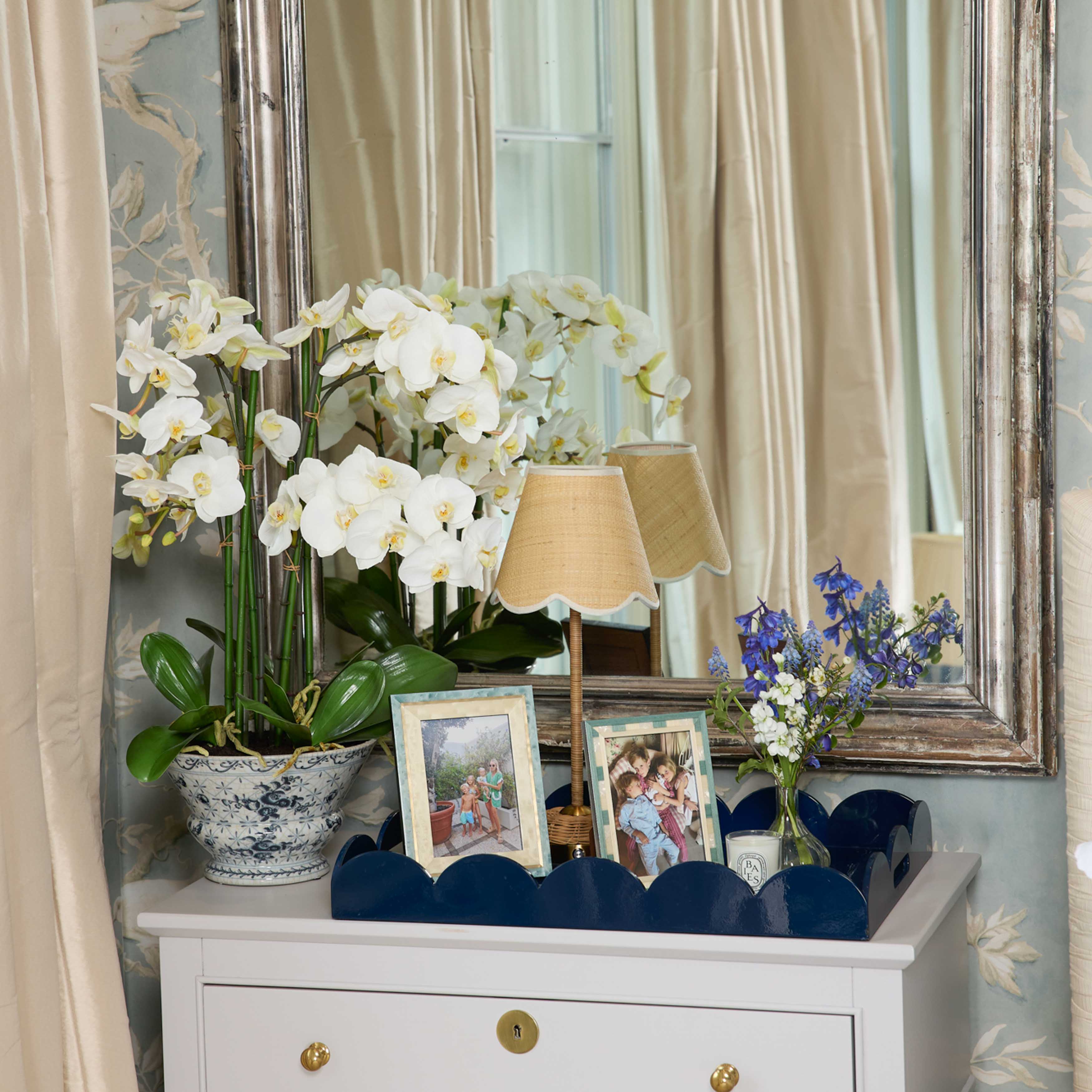 Decorative setup with white flowers, framed photos, and a lamp on a white cabinet.