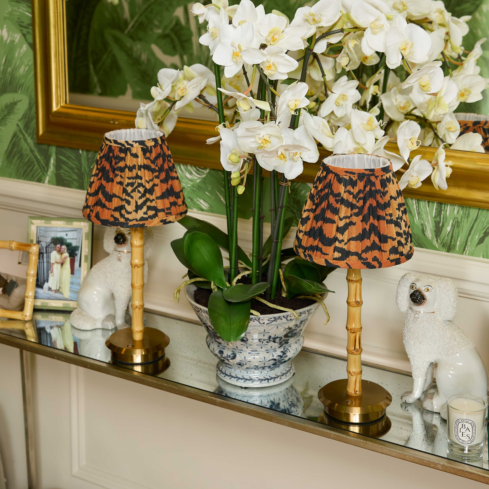 Decorative table with two small lamps, a potted plant, and a framed photo on a reflective surface.