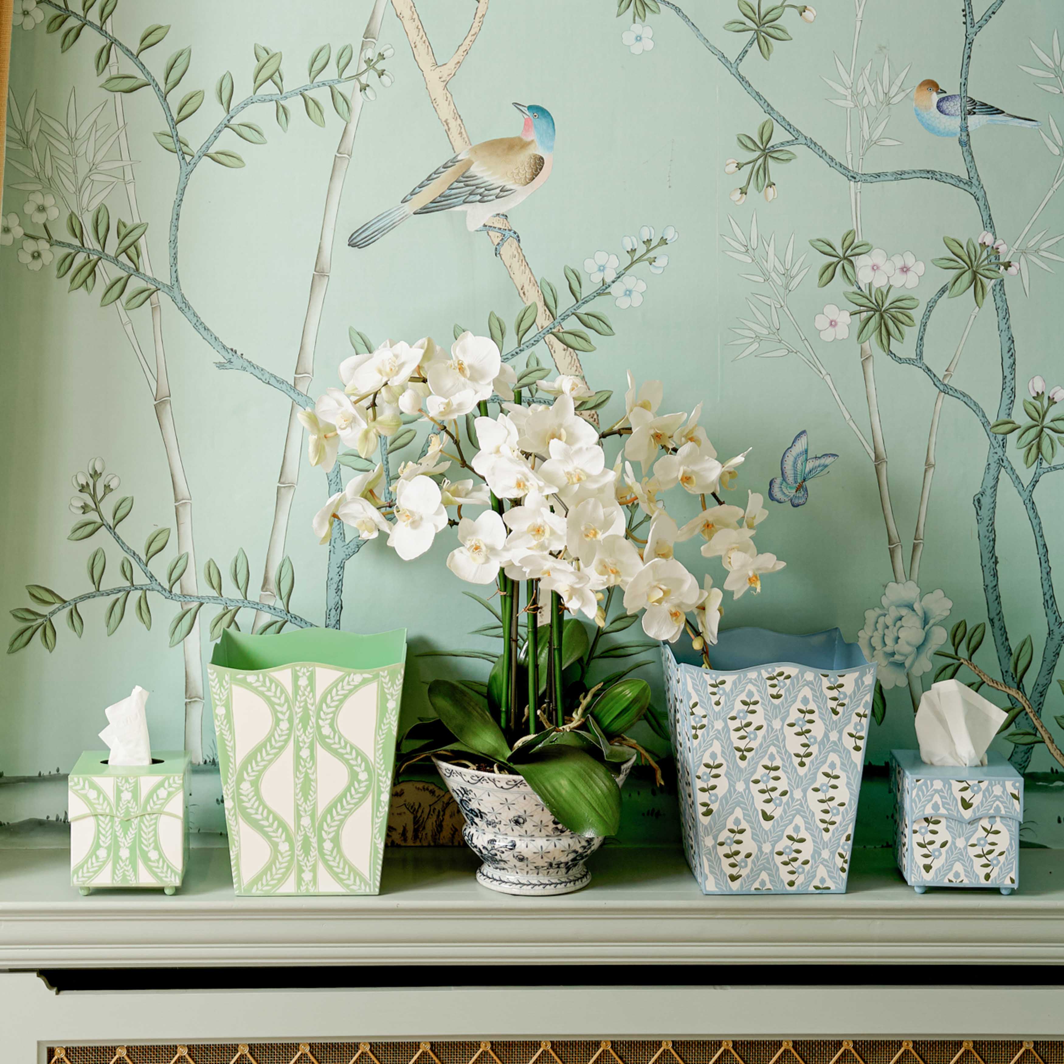 Decorative scene with white orchids, patterned vases, and tissue boxes against a decorative wall.