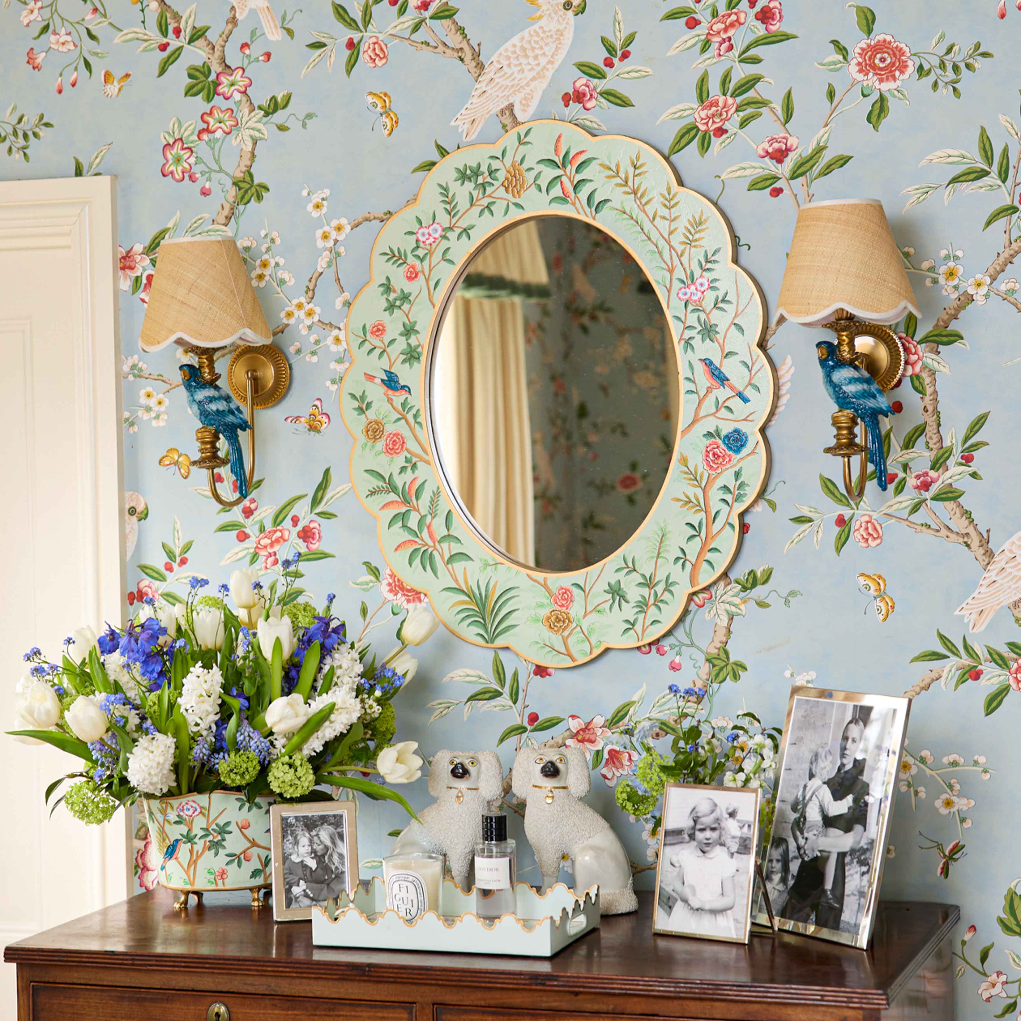 Decorative room interior with floral wallpaper, mirror, and floral arrangements.
