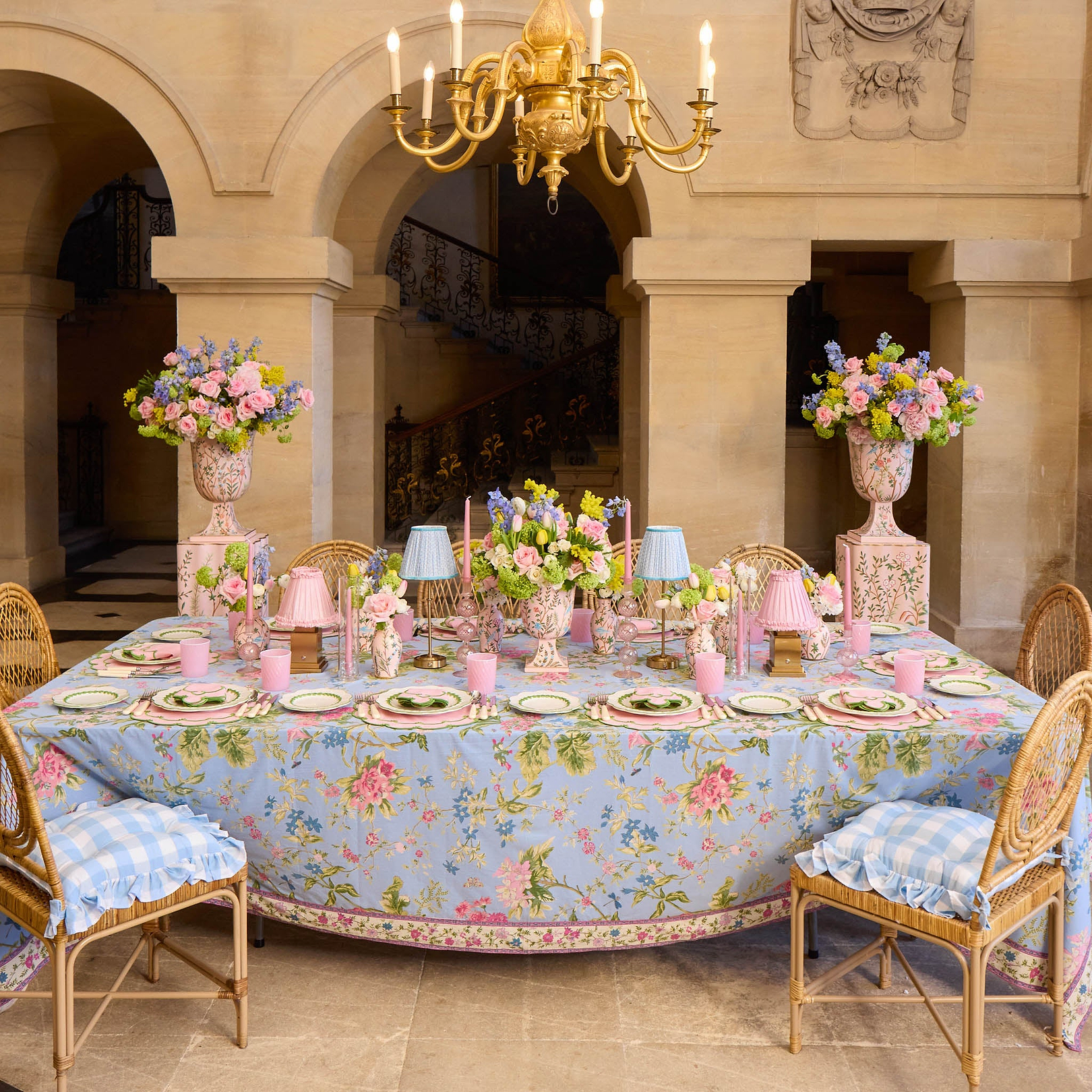 Elegant dining table setting with floral tablecloth and chairs in a grand room.