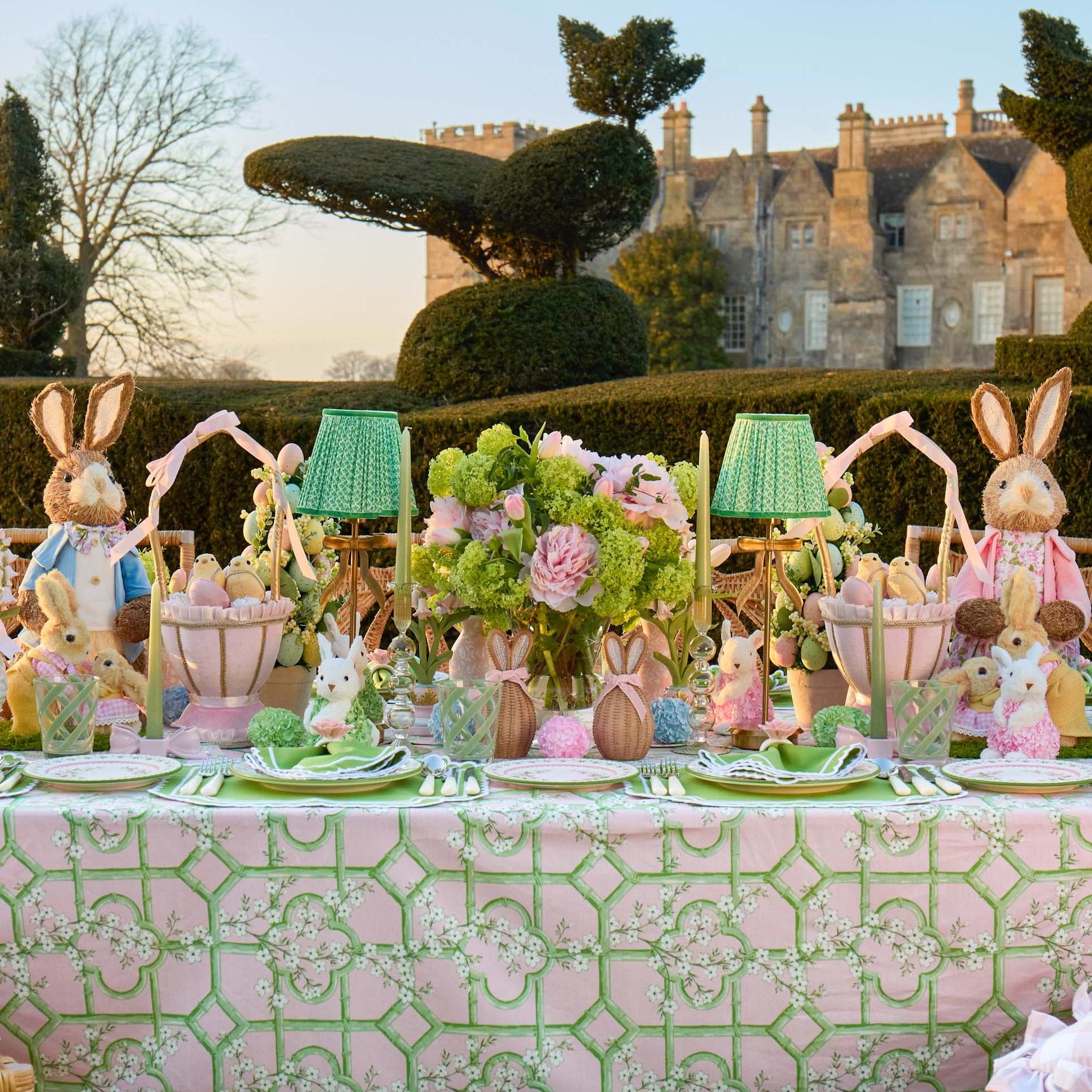 Easter-themed table setting with decorative bunnies and flowers in a garden.