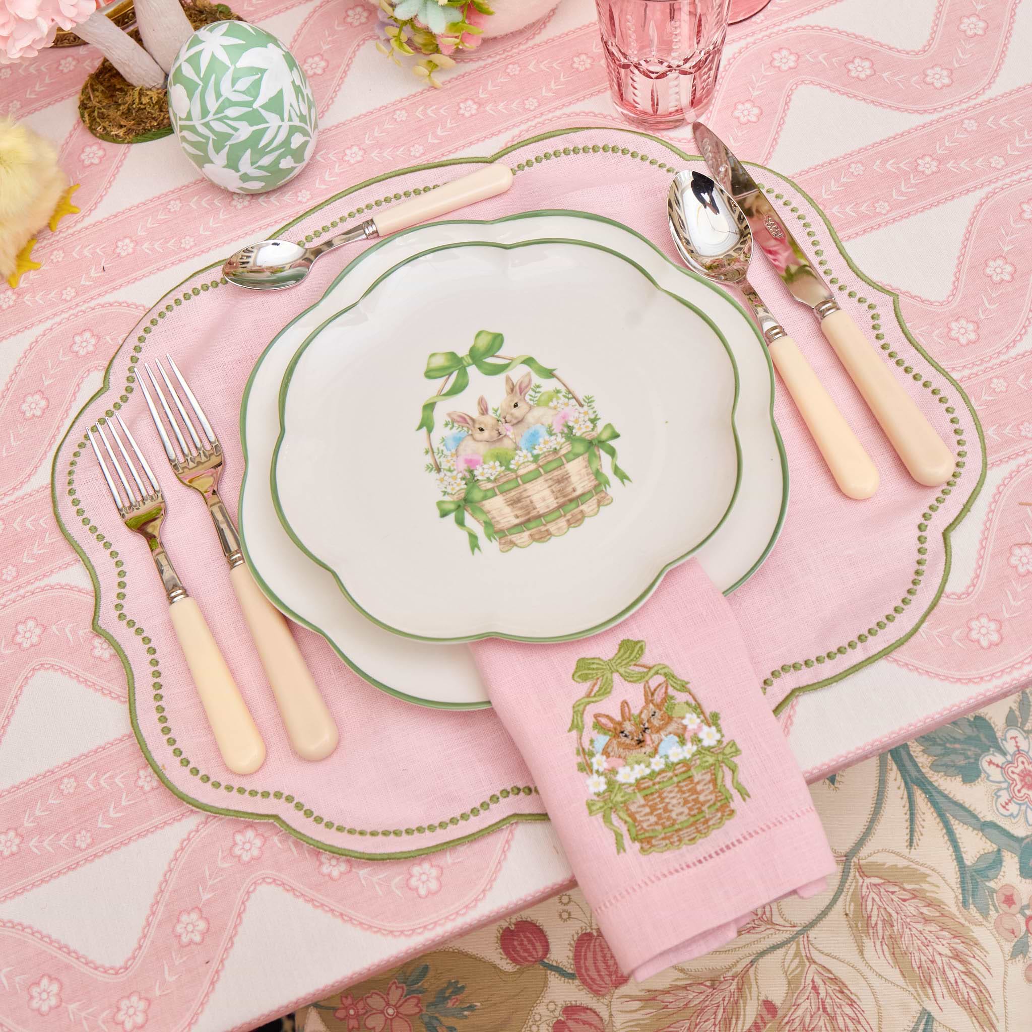 Easter-themed table setting with decorative plates, napkins, and cutlery on a pink tablecloth.