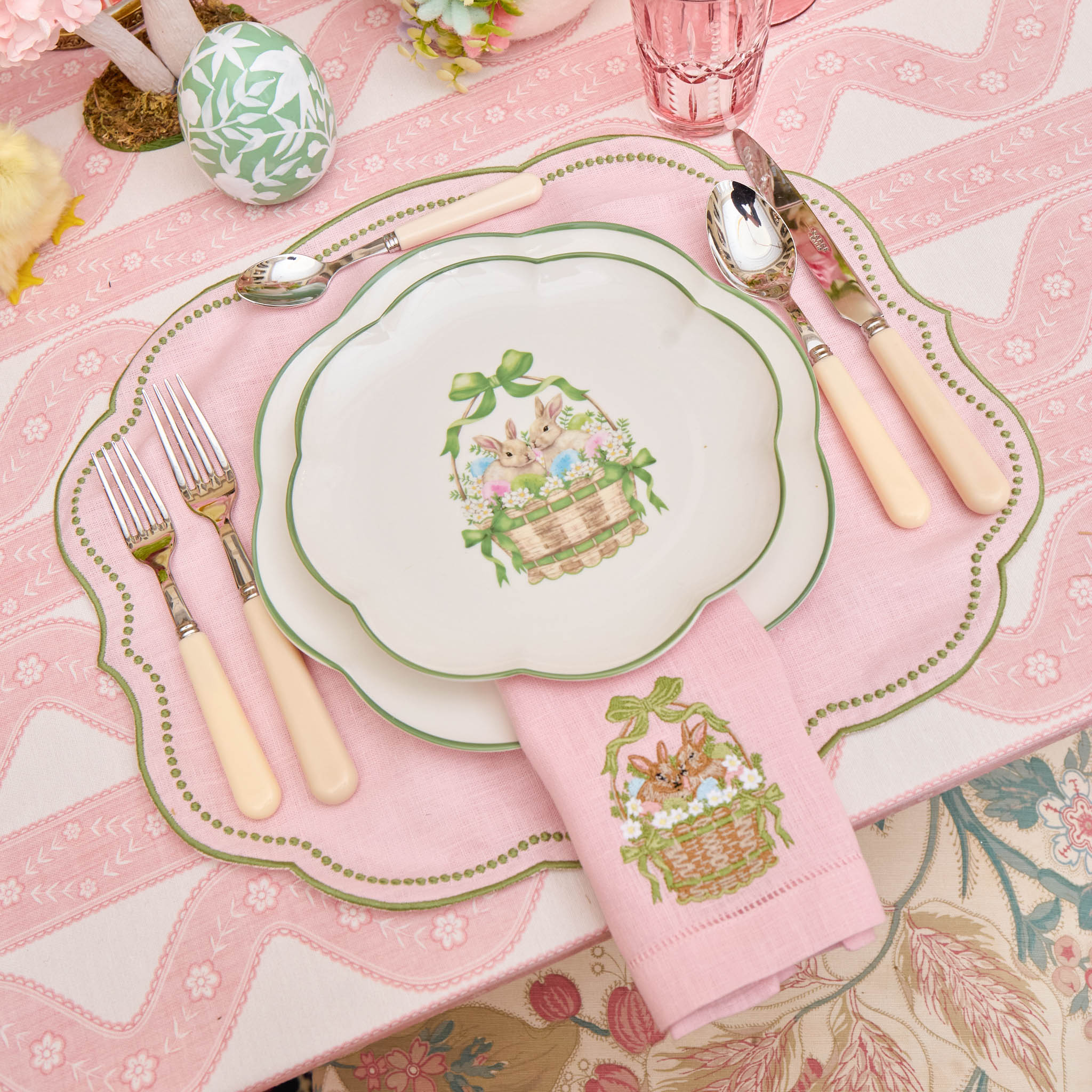 Easter-themed table setting with decorative plates, napkins, and cutlery on a pink tablecloth.