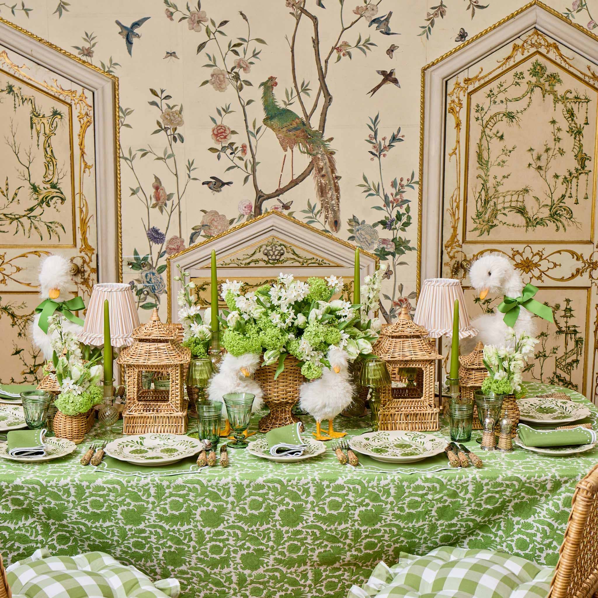 Decorative table setting with floral arrangements, lanterns, and birds in a room with ornate wallpaper.