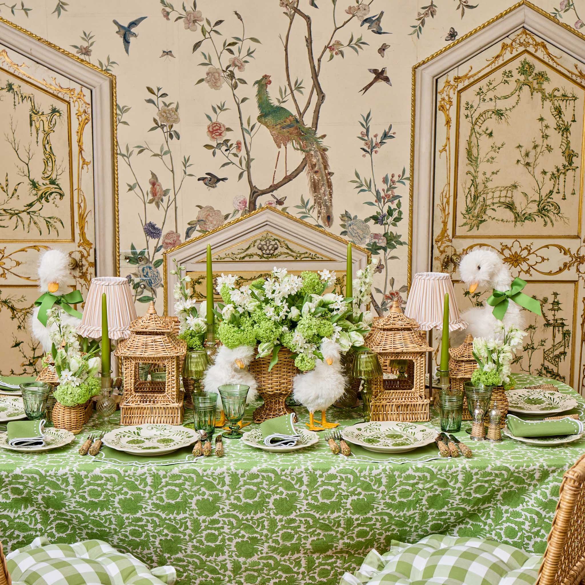 Decorative table setting with floral arrangements, lanterns, and birds in a room with ornate wallpaper.
