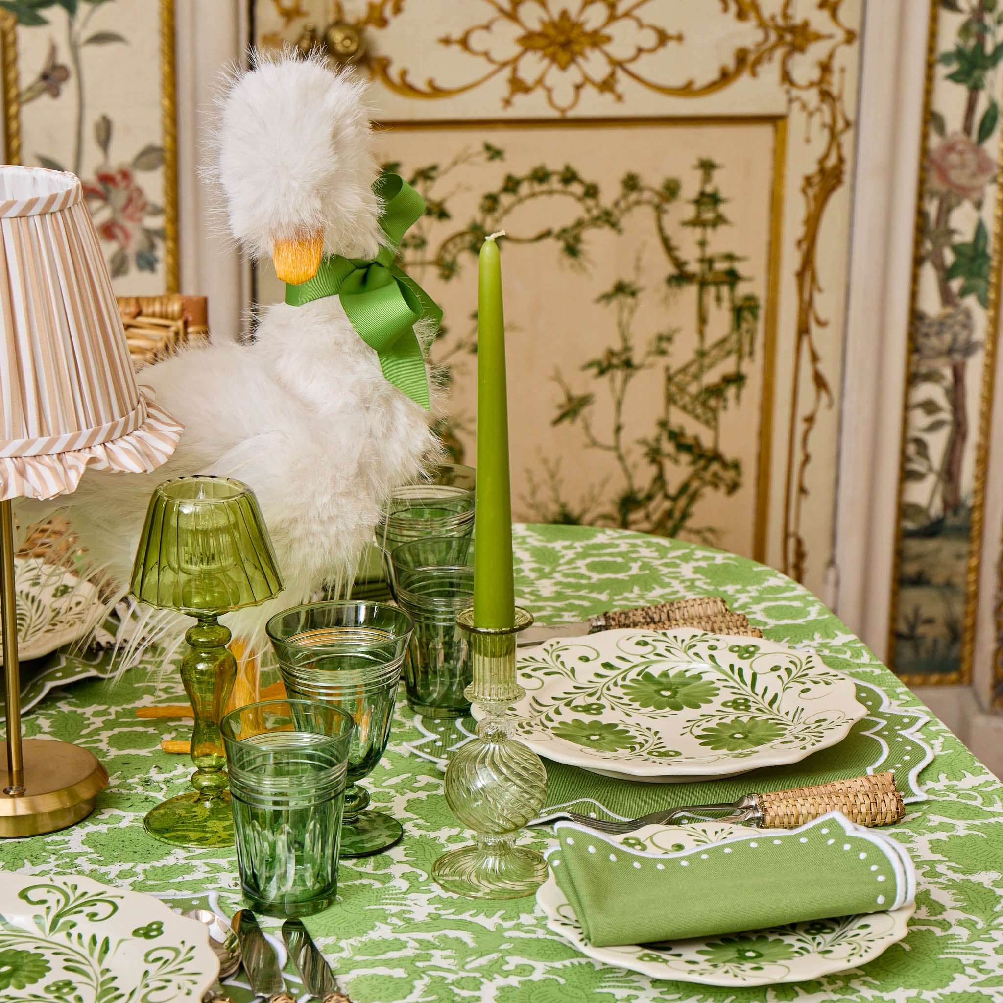 Decorative table setting with green tablecloth, glasses, candle, and napkin on a patterned wall background.