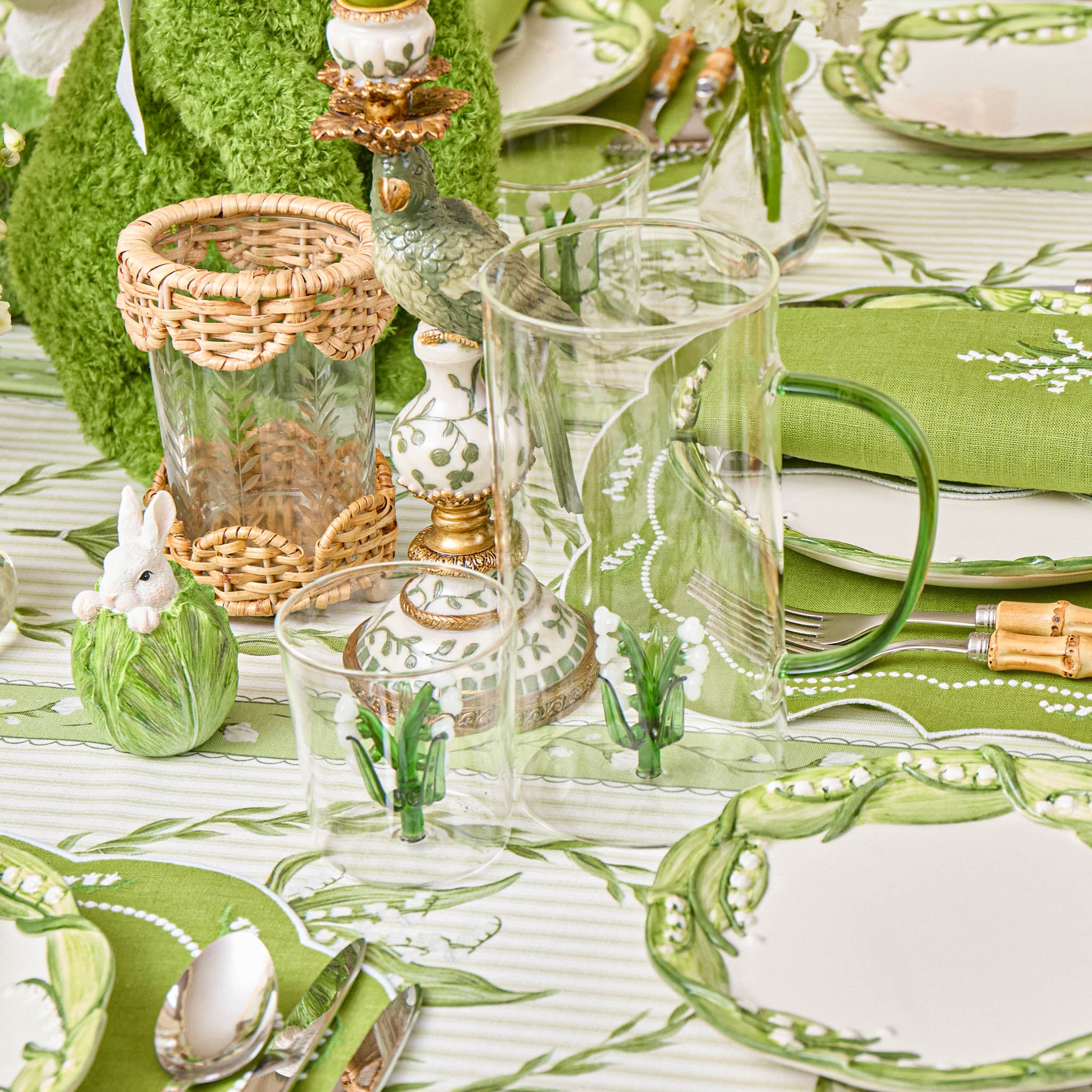 Easter-themed table setting with green and white decor, including plates, glasses, and decorative items.