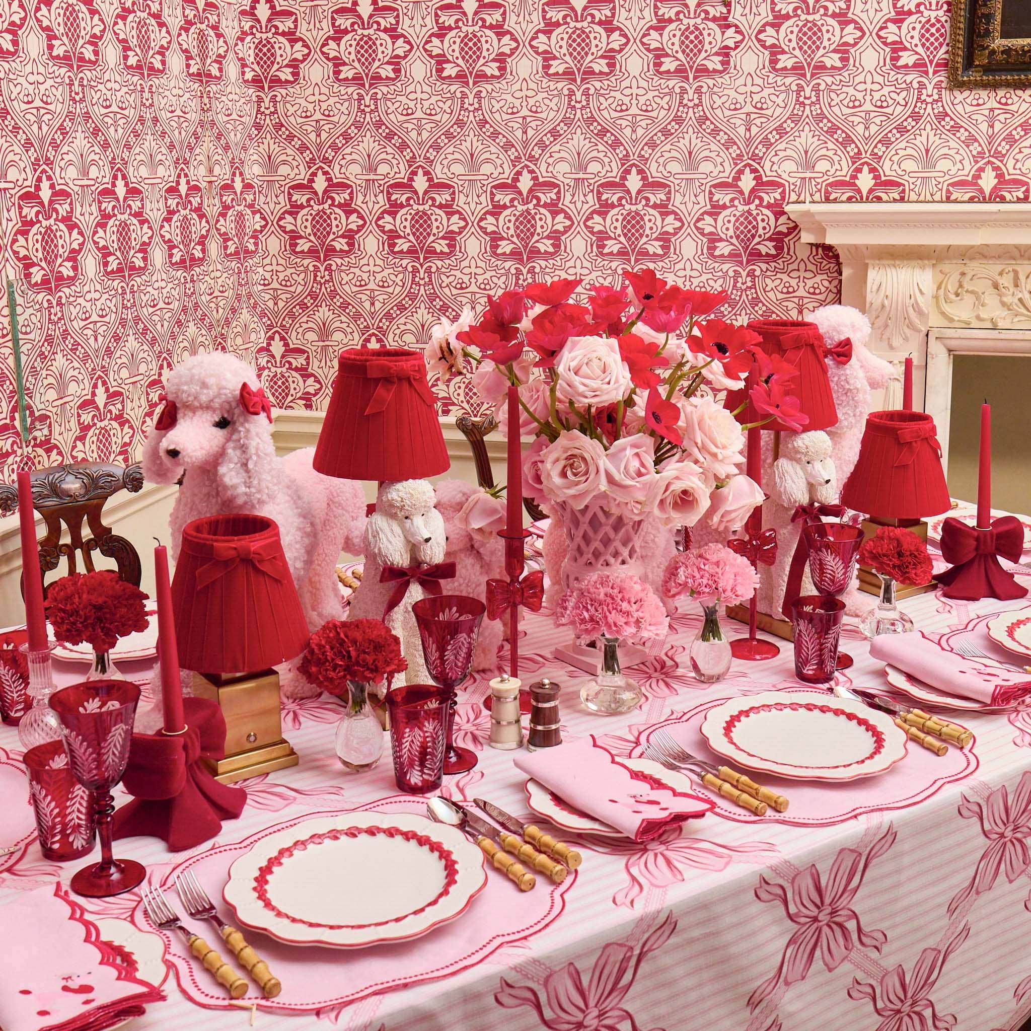 Decorative table setting with red and pink elements in a room with patterned wallpaper.