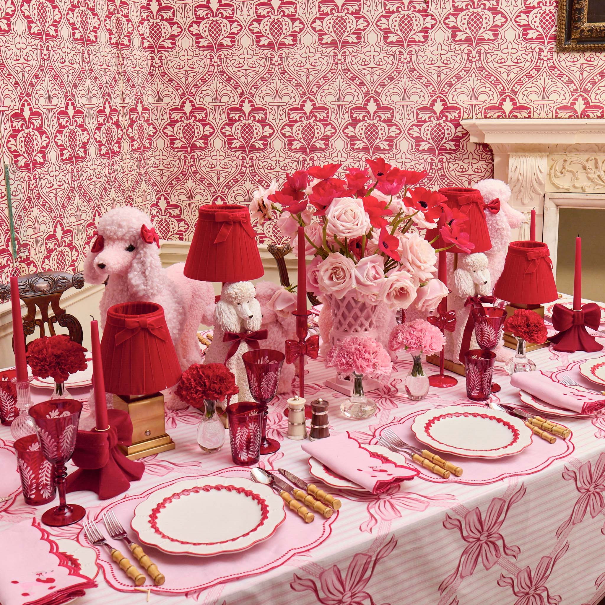 Decorative table setting with red and pink elements in a room with patterned wallpaper.