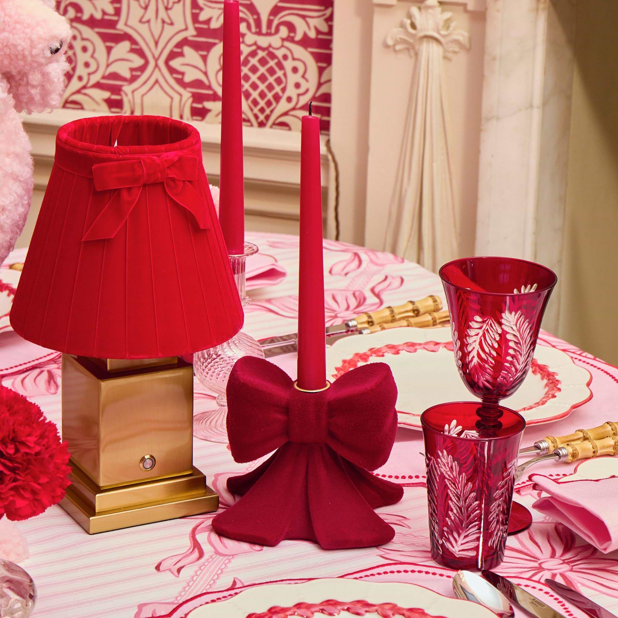 Decorative table setting with red lamp, candles, and glassware on a patterned tablecloth.