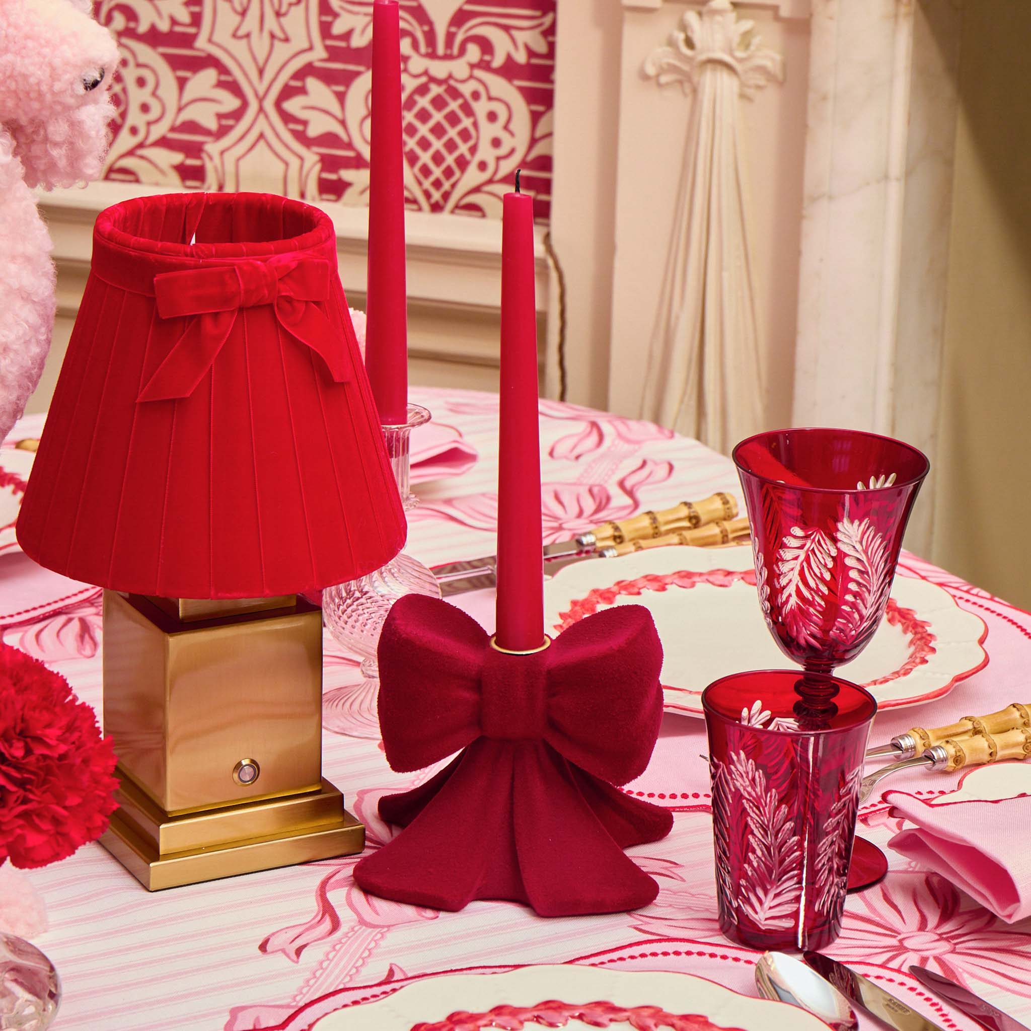 Decorative table setting with red lamp, candles, and glassware on a patterned tablecloth.
