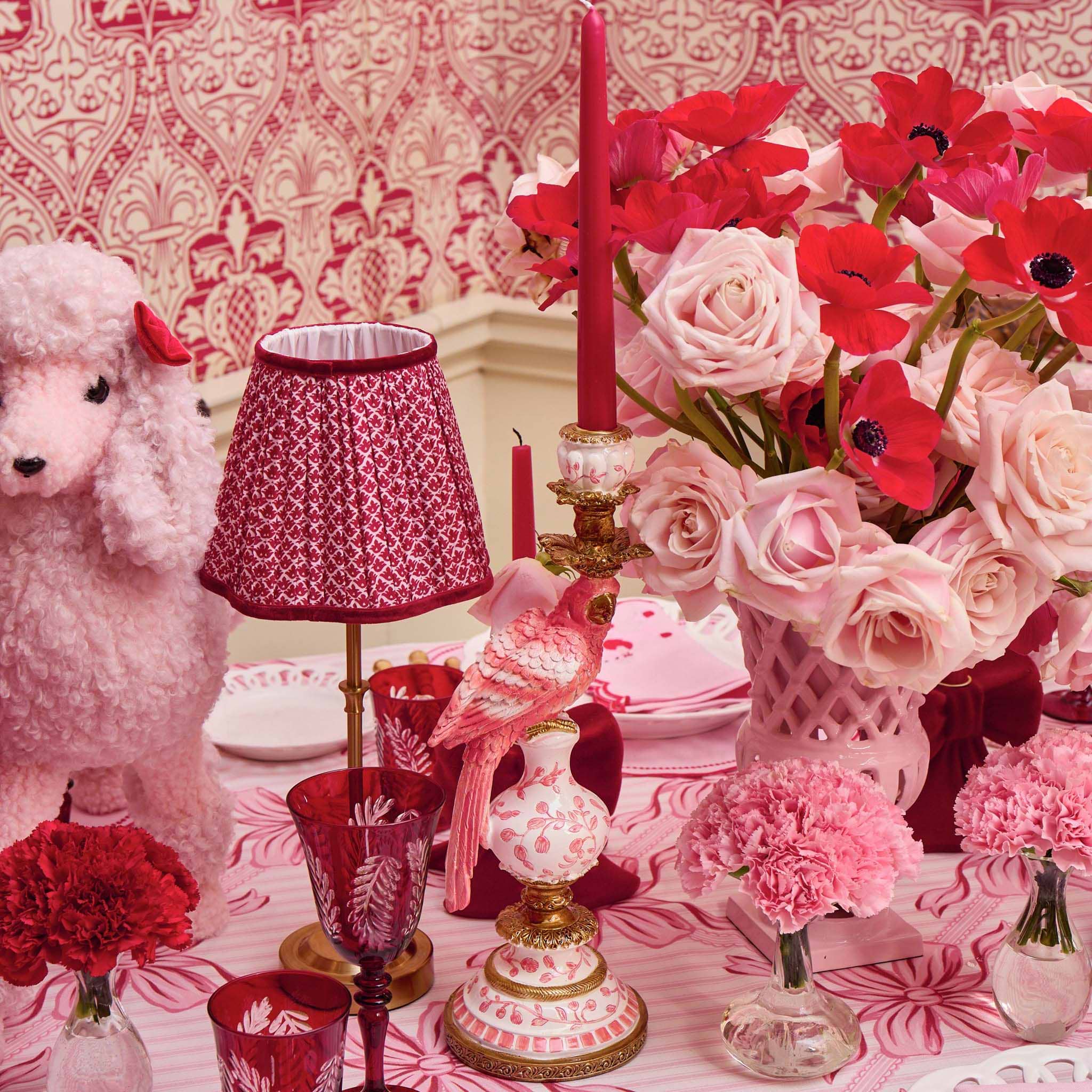 Decorative table setting with pink and red flowers, candles, and a small dog figurine.