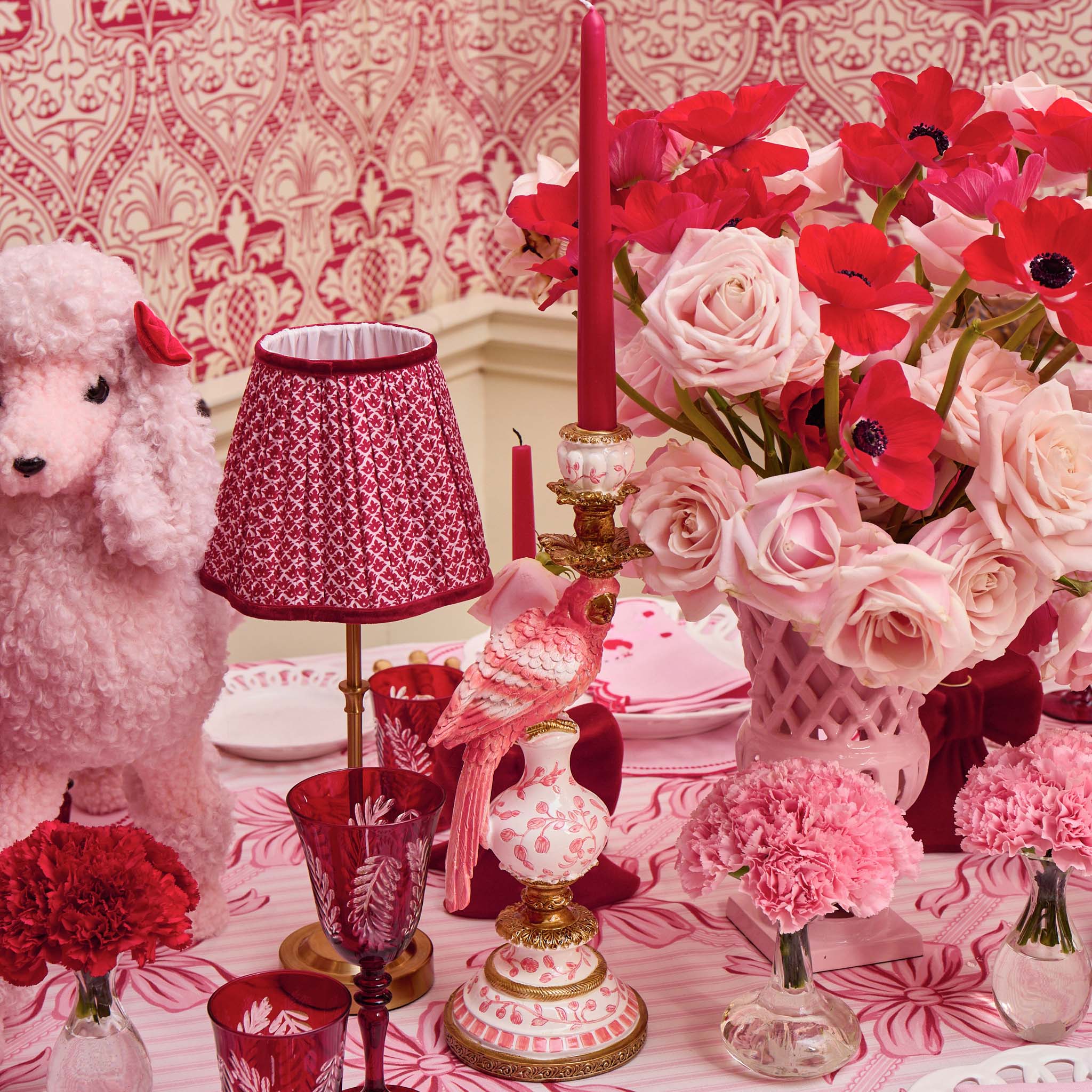 Decorative table setting with pink and red flowers, candles, and a small dog figurine.