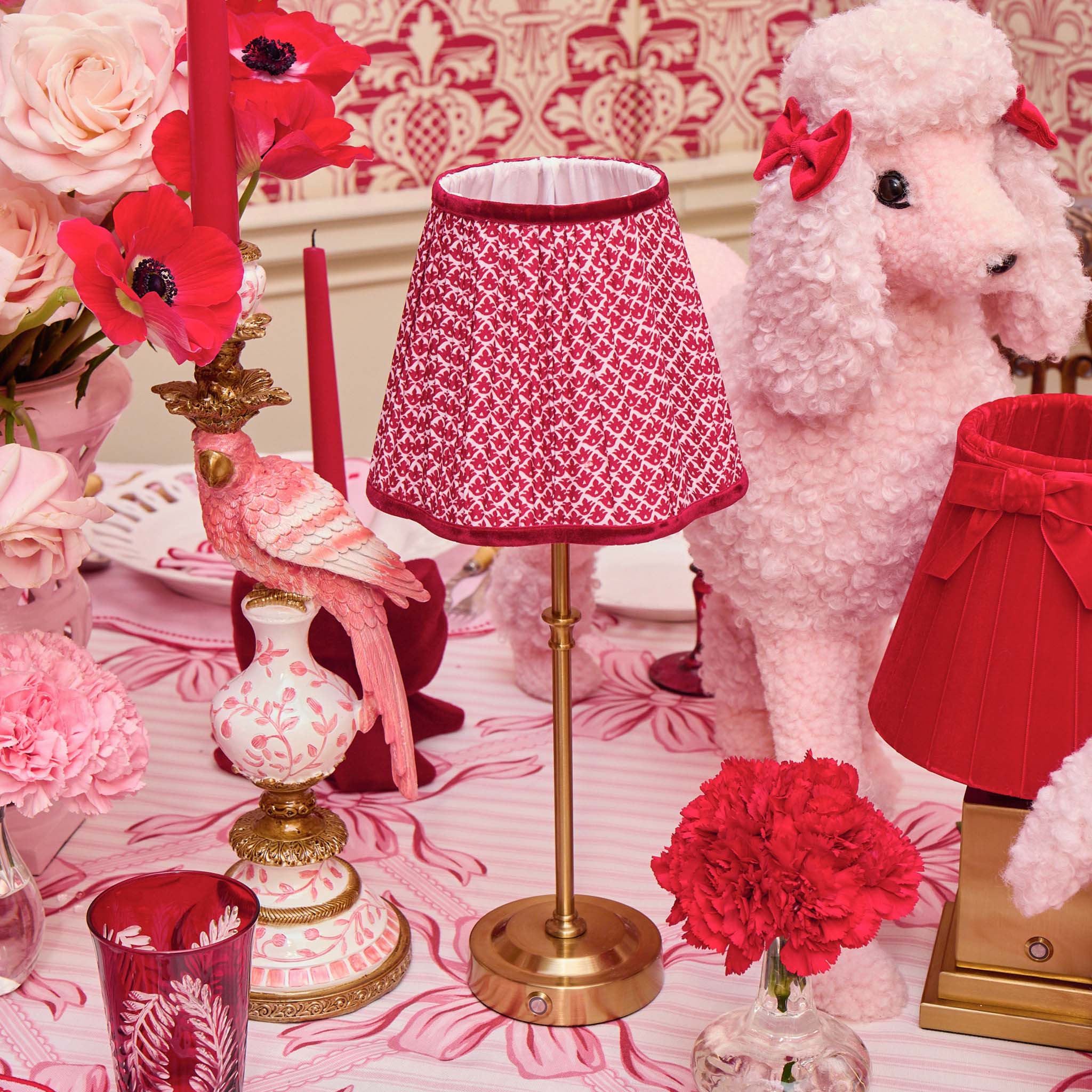 Decorative table setting with pink and red elements including a lampshade and flowers.