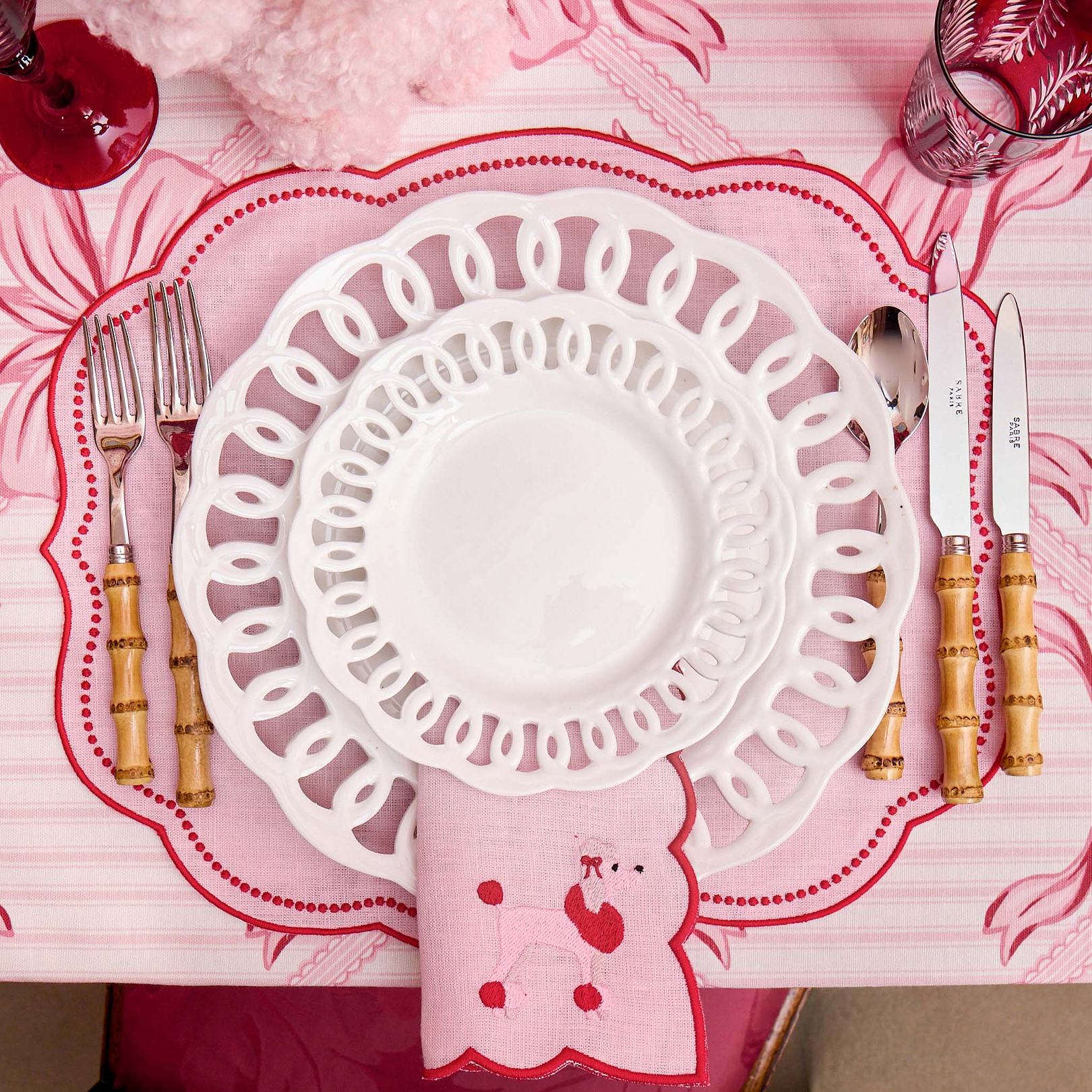 Decorative table setting with a pink placemat, white plate, and cutlery on a matching pink background.