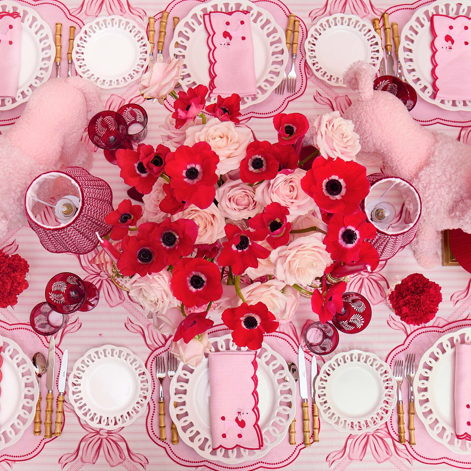 Decorative table setting with red and white flowers on a pink tablecloth.
