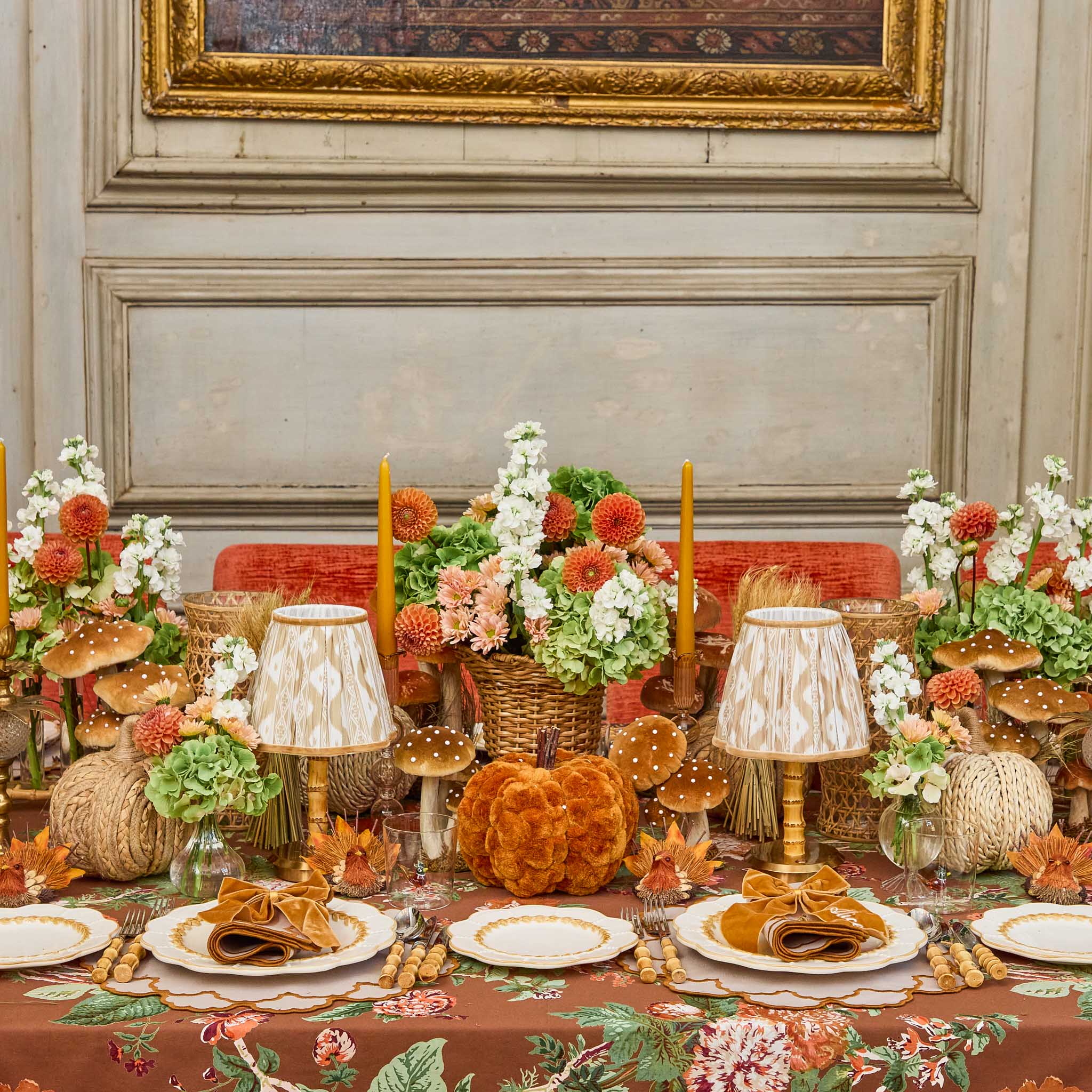 Decorative table setting with pumpkins, bamboo cutlery set, flowers, and lamps in a room with framed artwork on the wall.