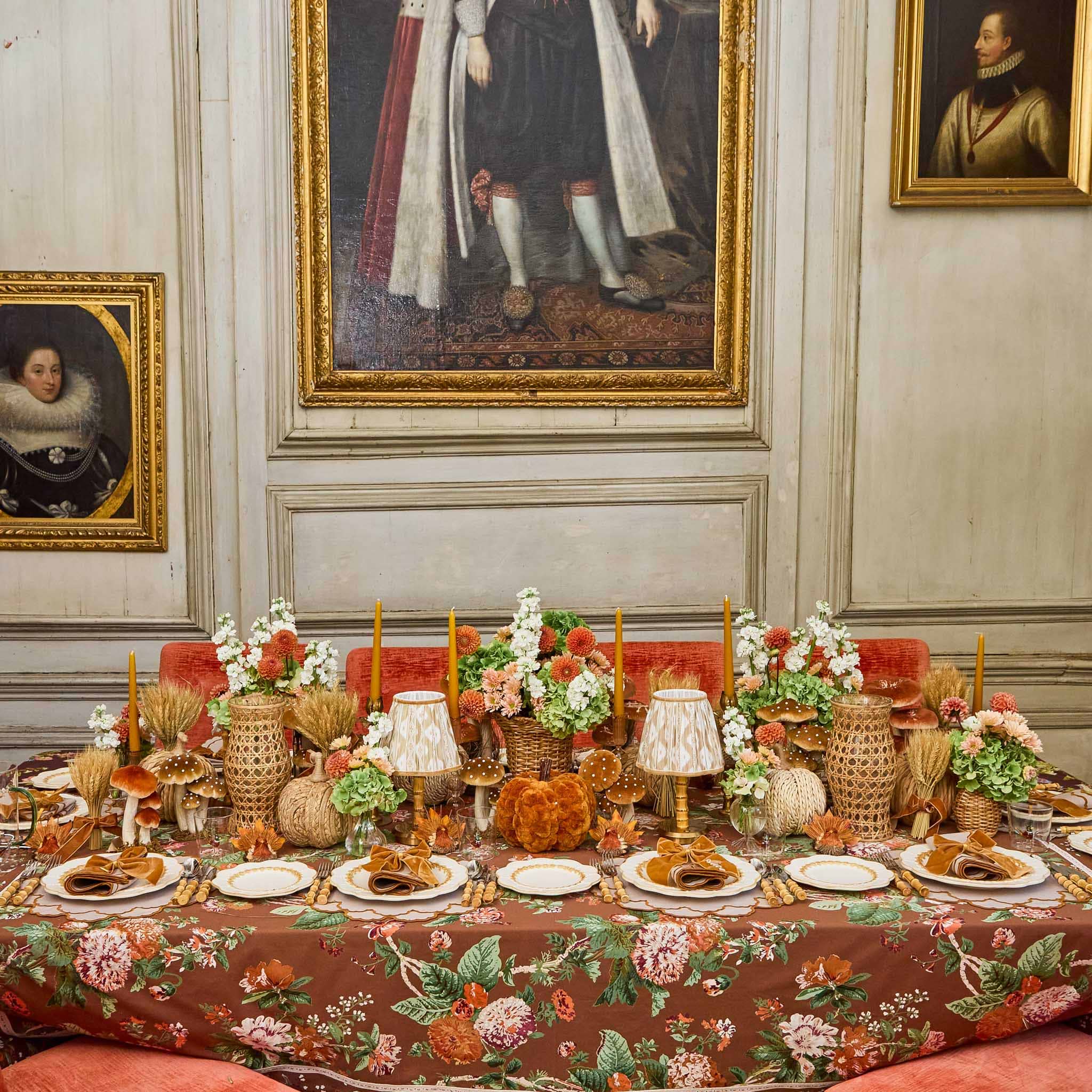 Decorative table setting with floral arrangements and bamboo cutlery set in a room with classical paintings on the wall.