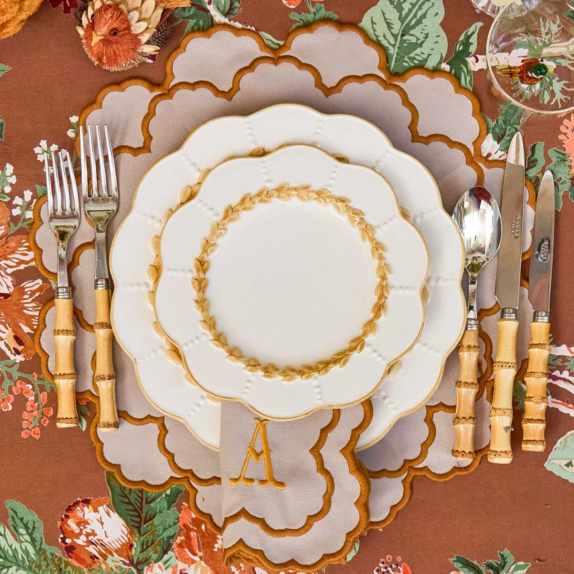 Decorative table setting with floral tablecloth, plates, bamboo cutlery set, and monogrammed placemat.