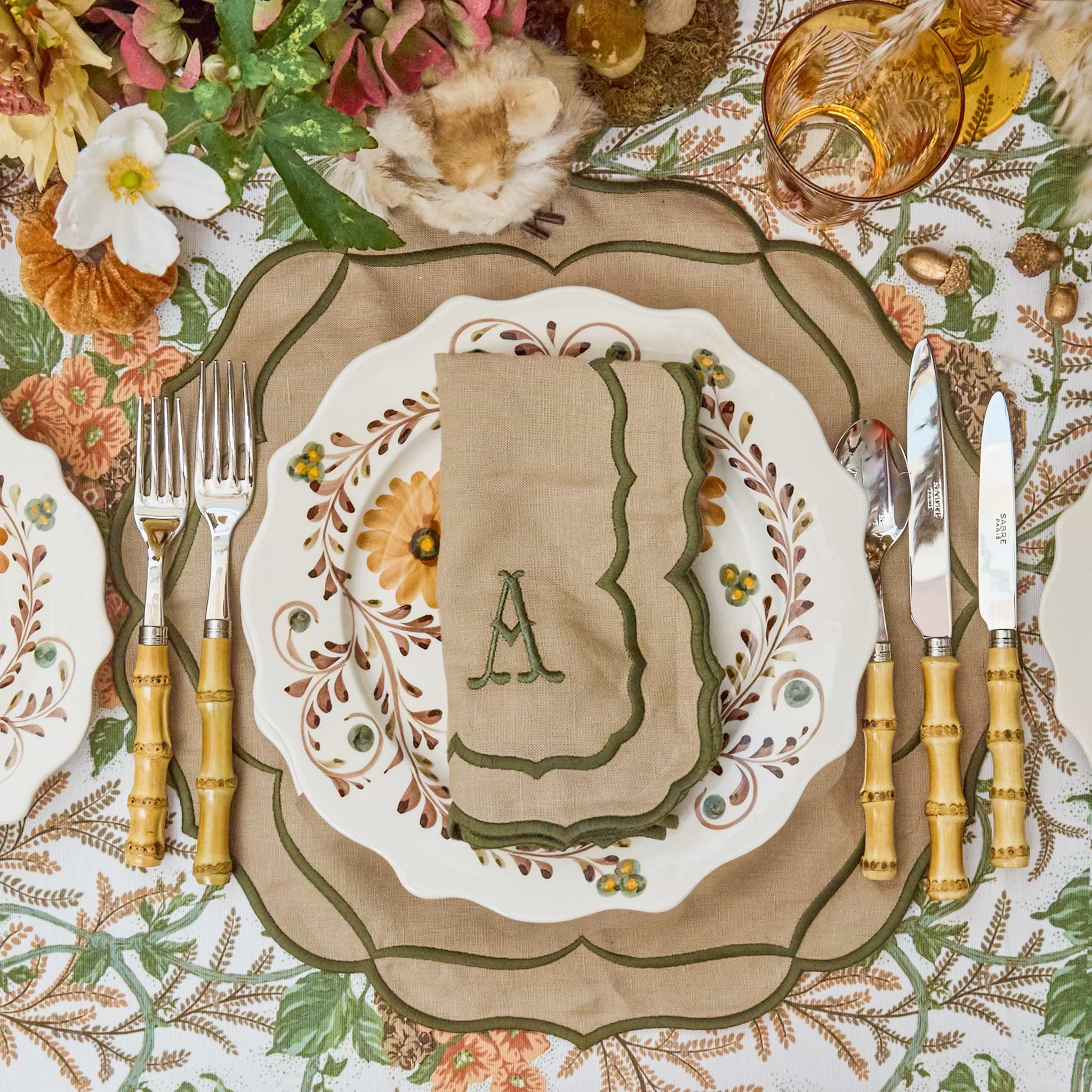 Decorative table setting with floral patterns, bamboo cutlery set, and a napkin with an 'A' monogram.