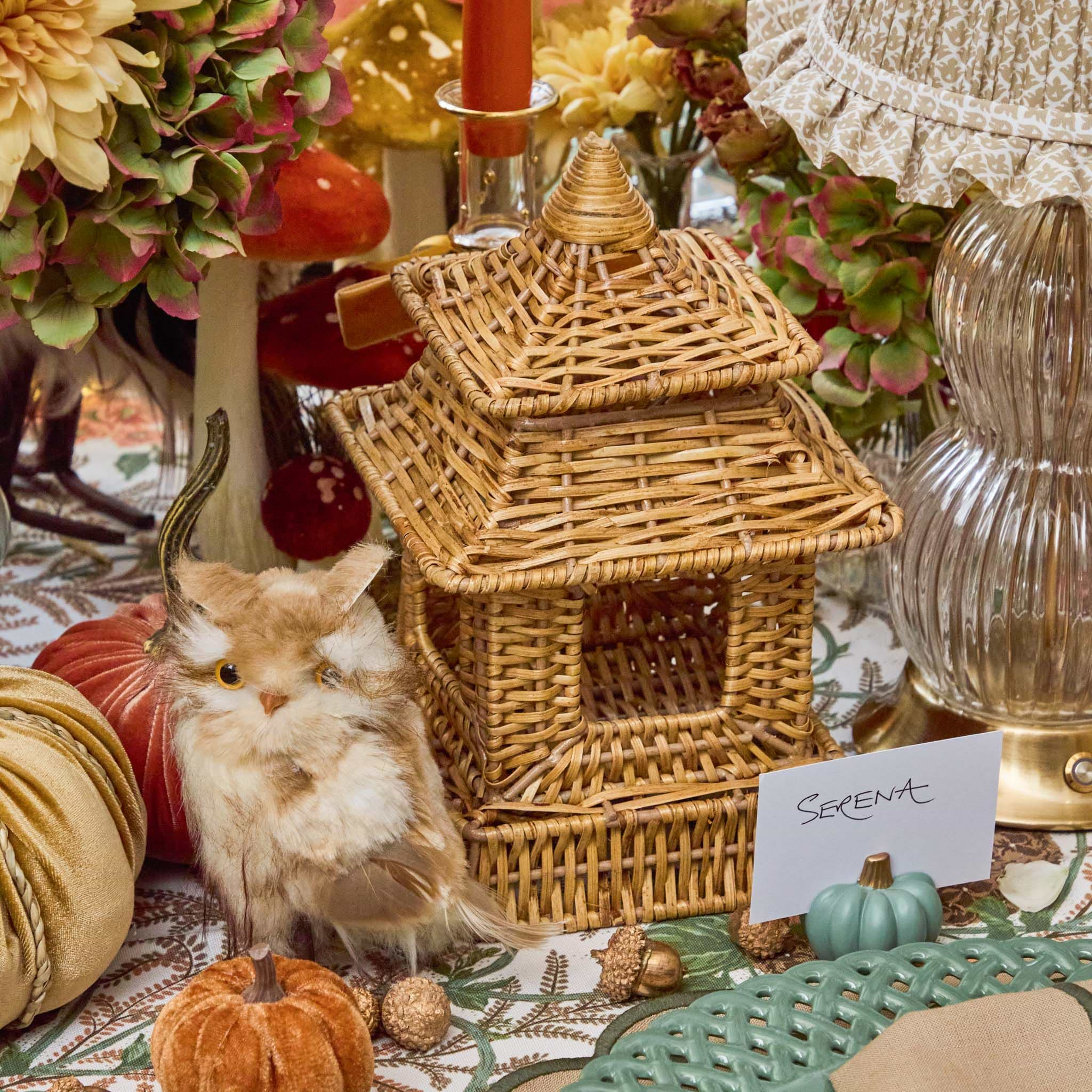 Decorative setting with a wicker pagoda, faux animal, and pumpkins on a table.