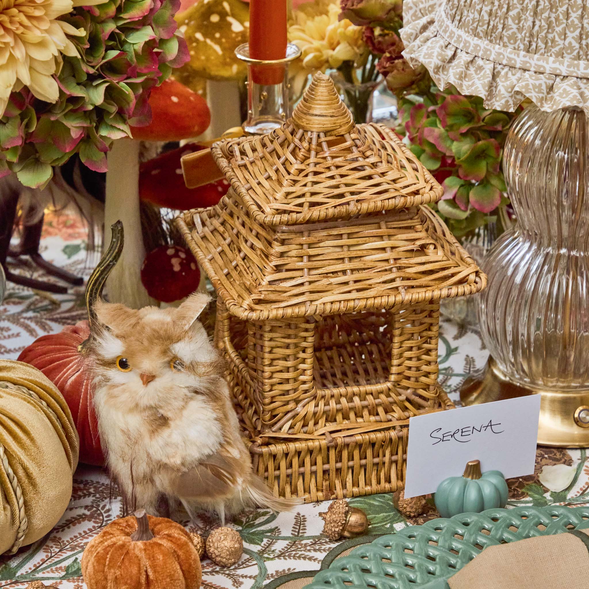 Decorative setting with a wicker pagoda, faux animal, and pumpkins on a table.