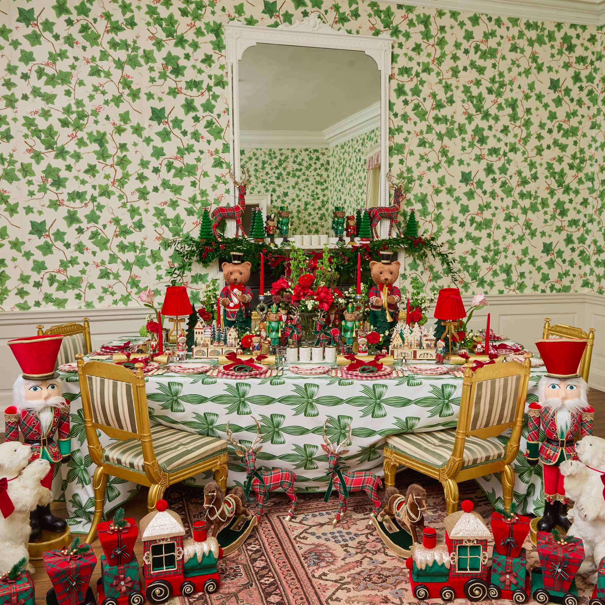 Decorative Christmas table setting with teddy bears, trains, and a patterned wall.